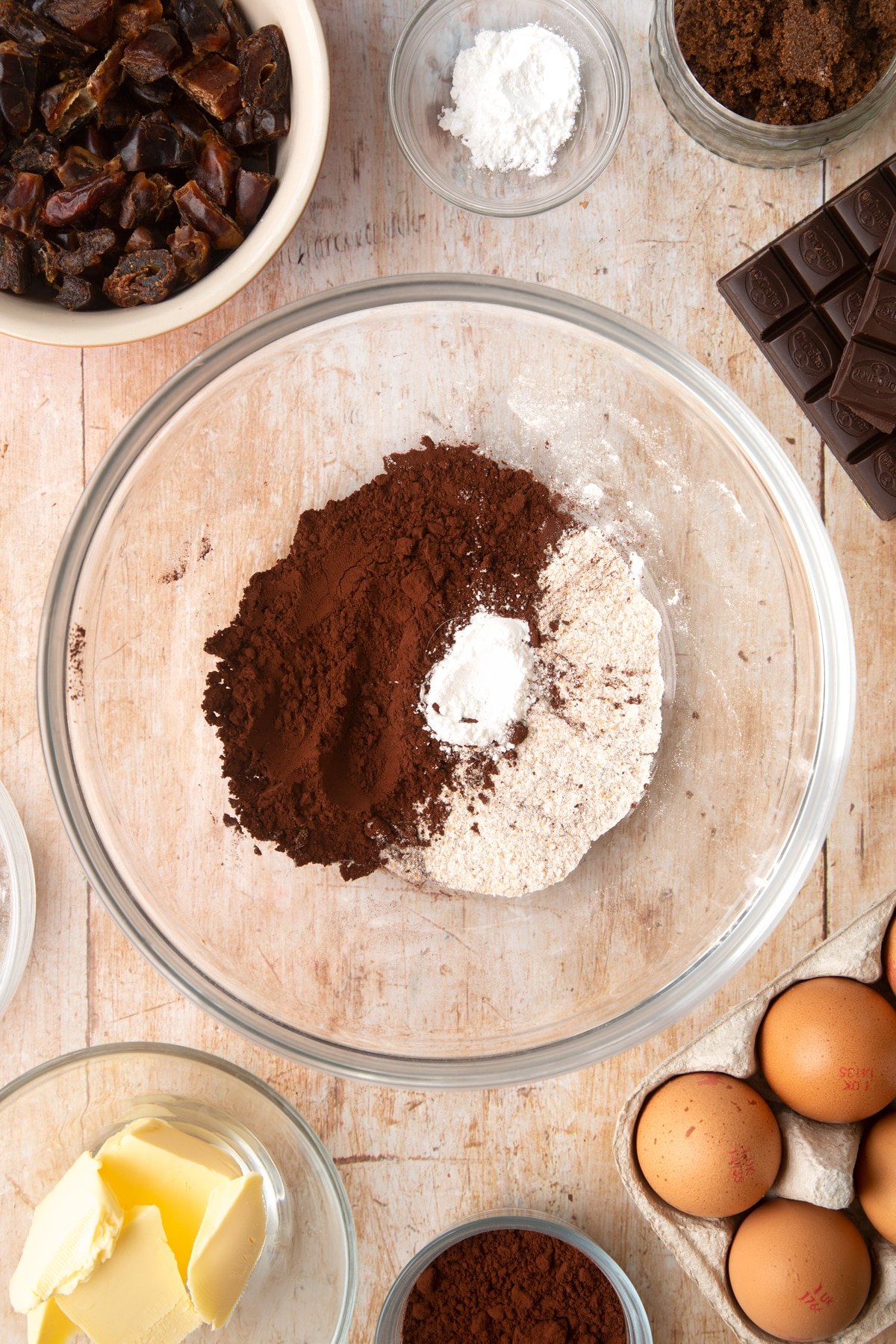 A mixing bowl containing cocoa, wholemeal flour and baking powder. Ingredients to make whole grain brownies surround the bowl.