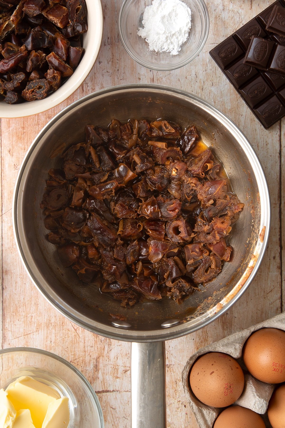 A sauce pan containing chopped dried dates simmered in water. Ingredients to make whole grain brownies surround the pan.