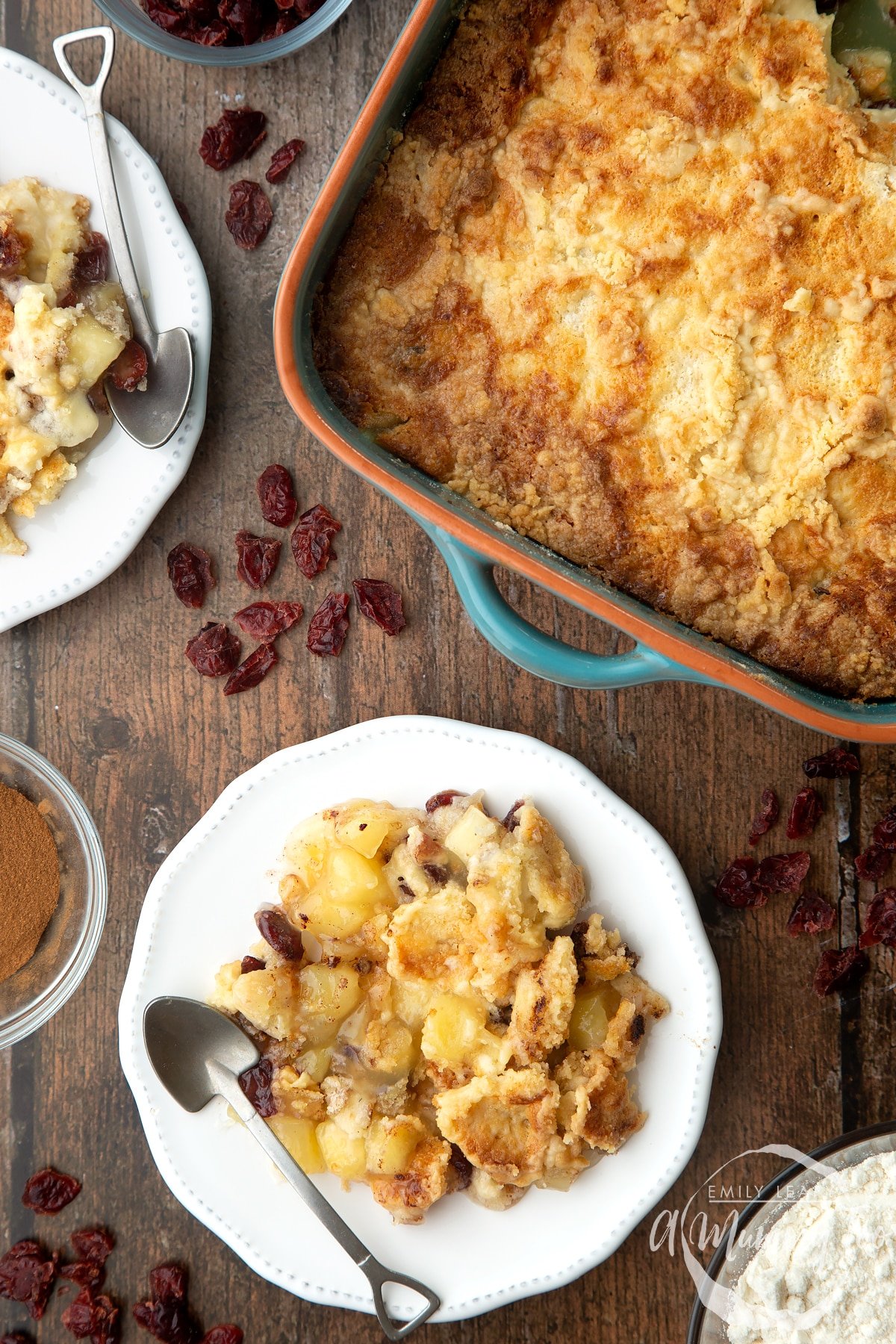 Apple cranberry dump cake served onto a small white plate. More Apple cranberry dump cake is shown in a tray to the side.