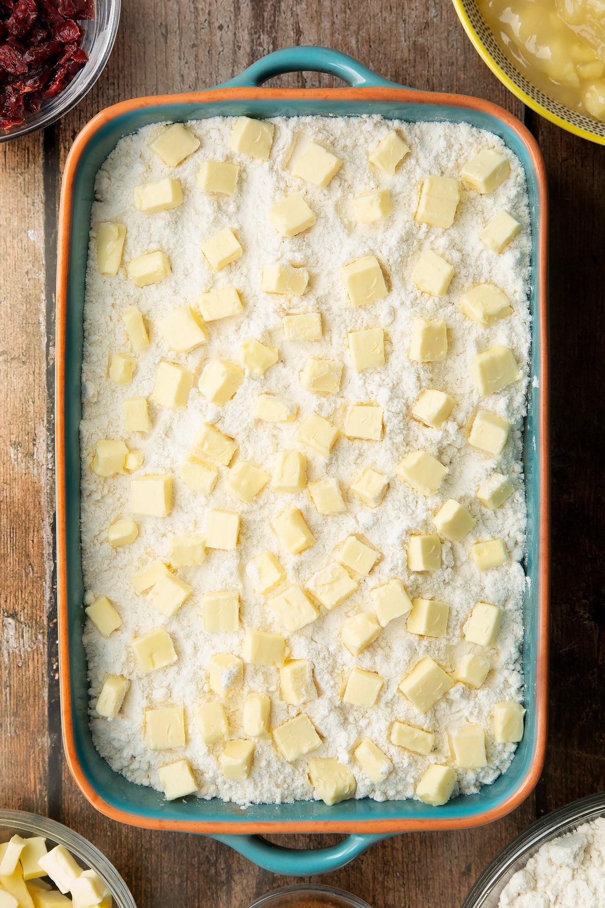 Tinned apple filling, dried cranberries, cinnamon and cake mix dotted with butter in a roasting tray.