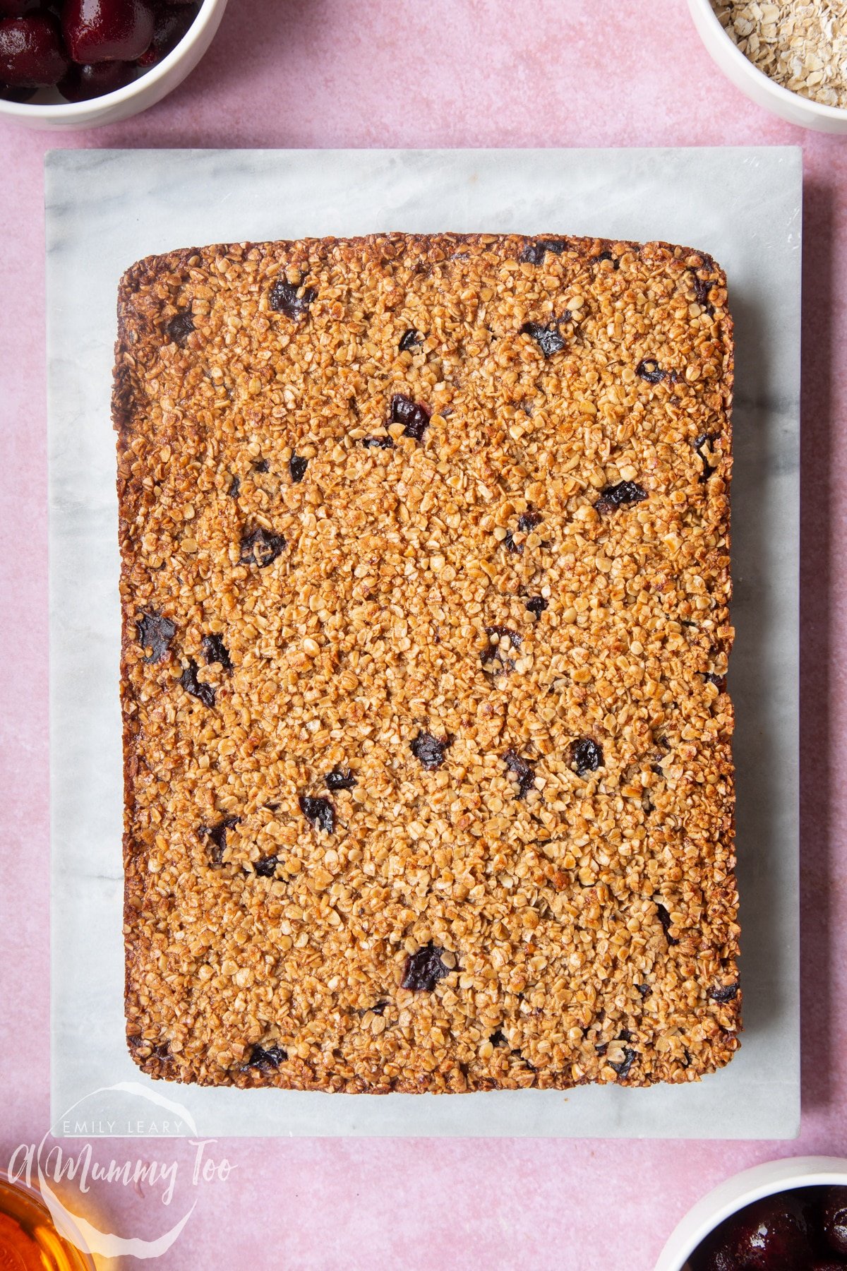 Overhead shot of cherry flapjacks on a marble chopping board with a mummy too logo in the lower-left corner