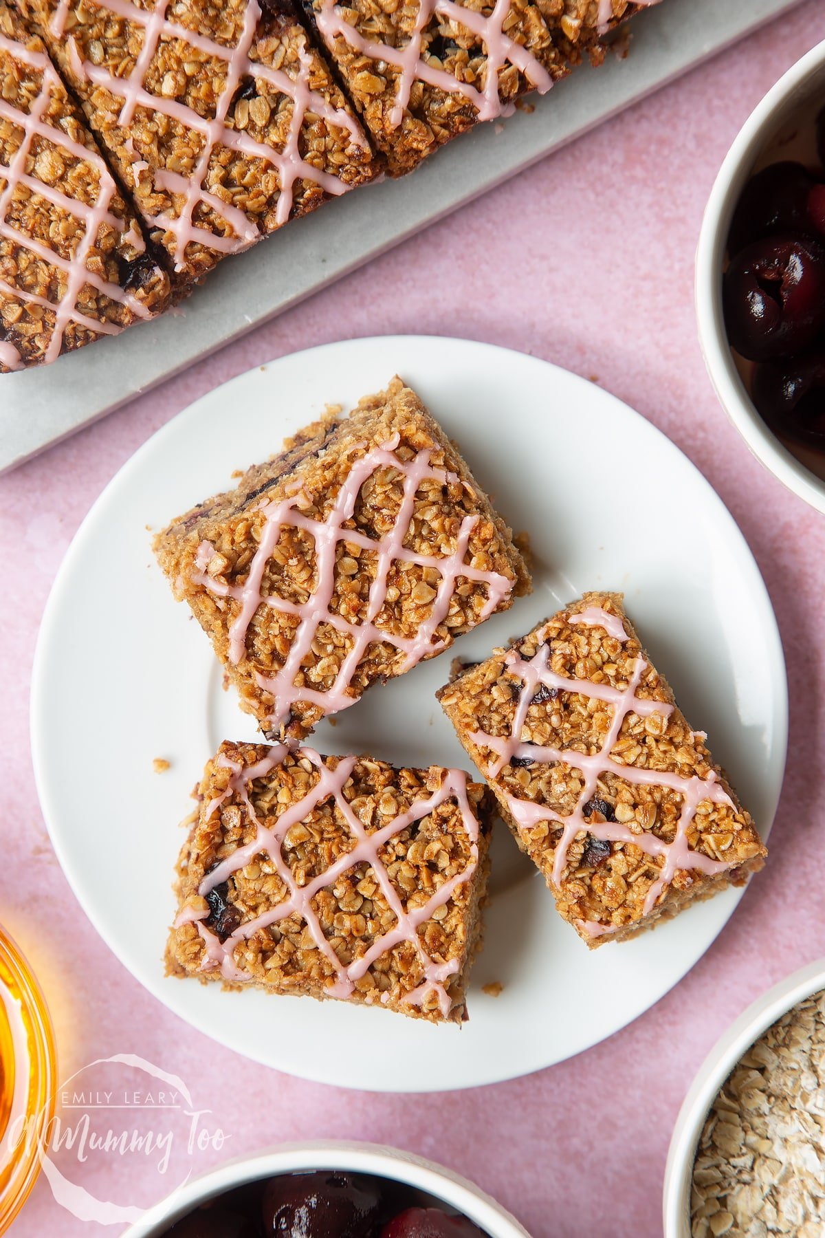 Overhead shot of cherry flapjacks topped with pink icing served on a white plate with a mummy too logo in the lower-left corner