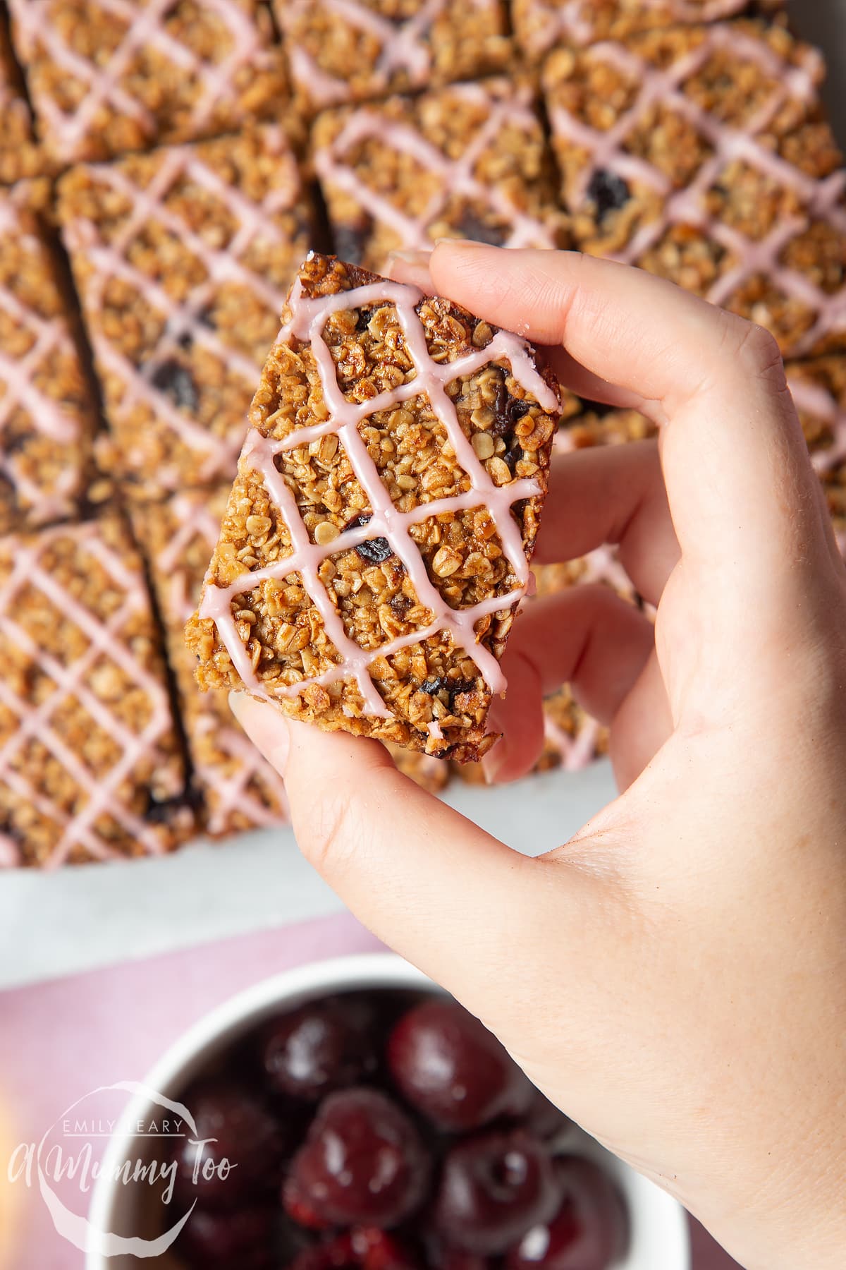 Overhead shot of a hand holding a cherry oat bar with a mummy too logo in the lower-left corner