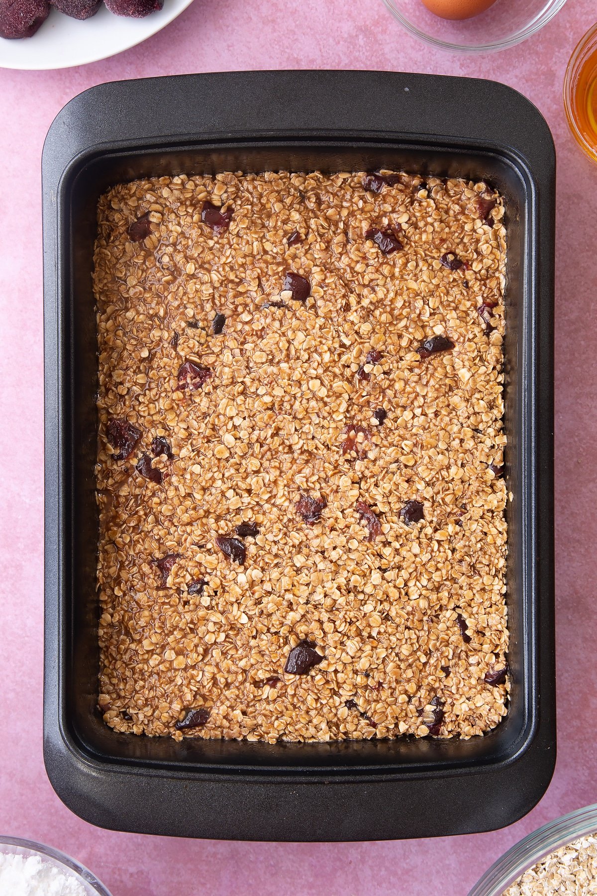 Overhead shot of flattened oats mix in a black baking tin