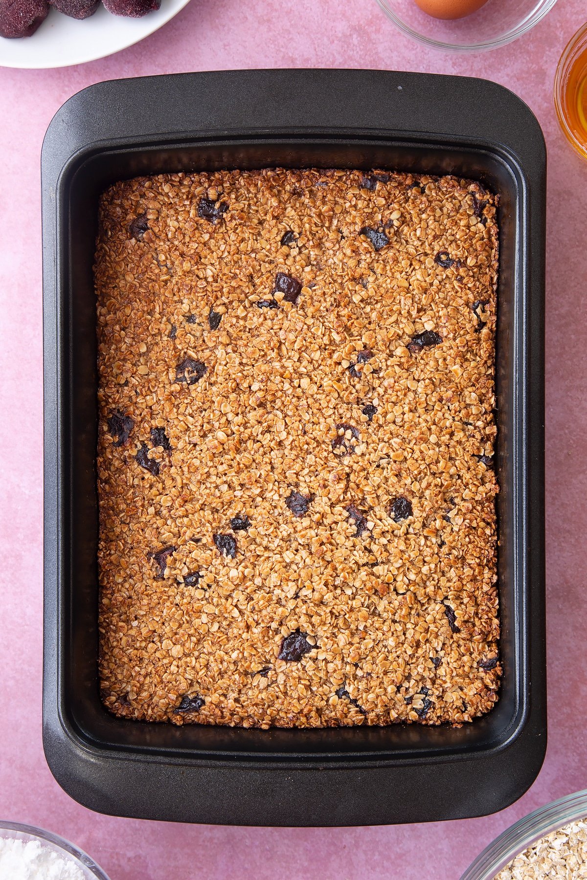 Overhead shot of cherry flapjacks in a black baking tin