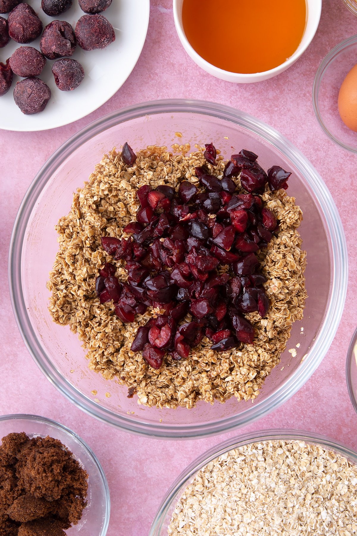 Overhead shot of oats mix with chopped cherries on top in a large clear bowl