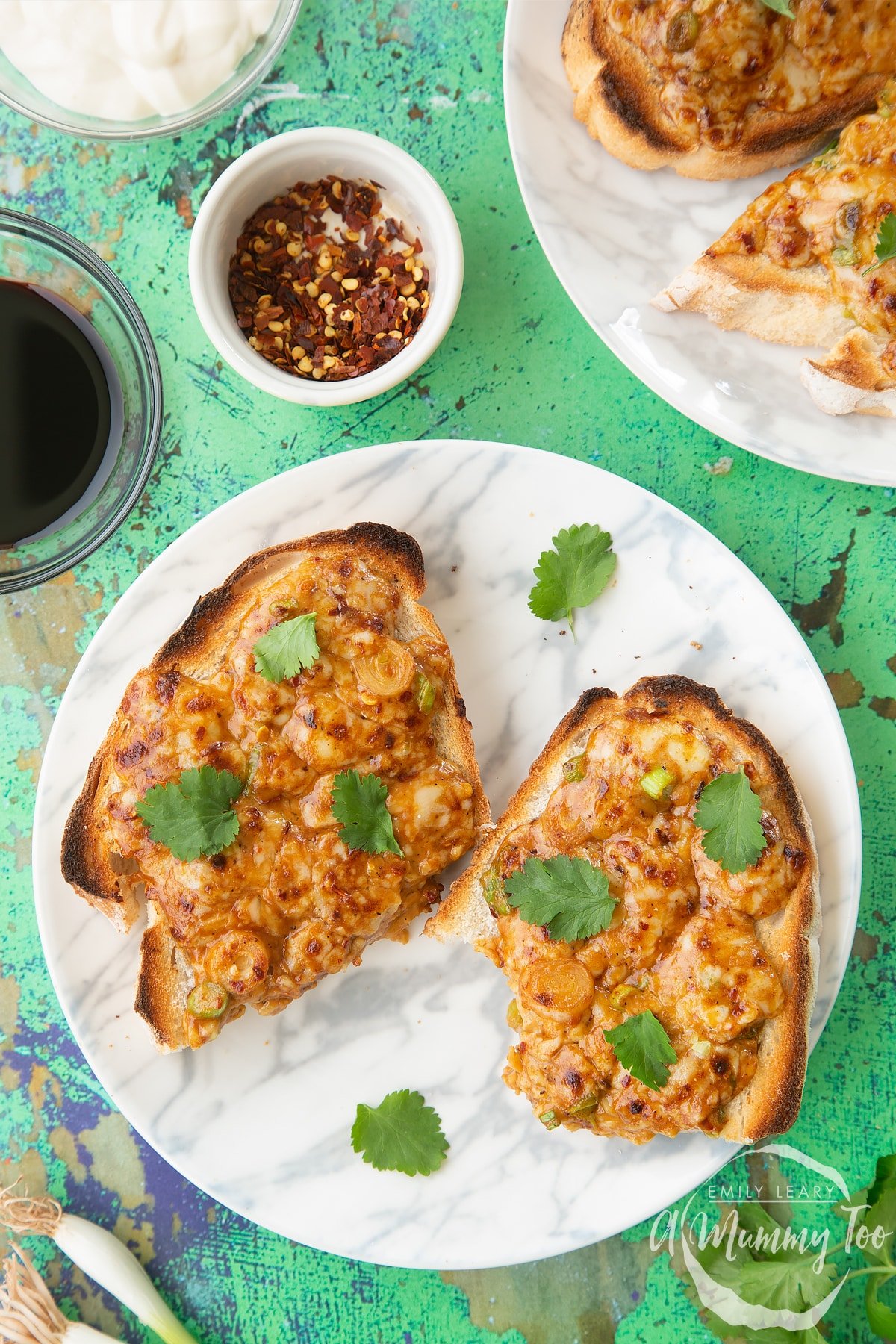 Two pieces of chilli cheese toast  on a white marbled plate, scattered with coriander. One has a bite out of it.