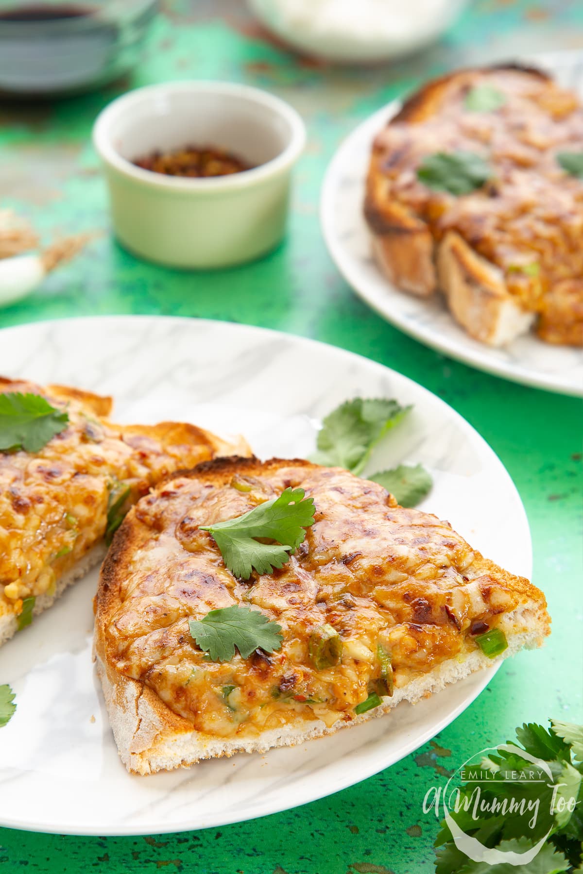 Two pieces of chilli cheese toast on a white marbled plate, scattered with coriander.