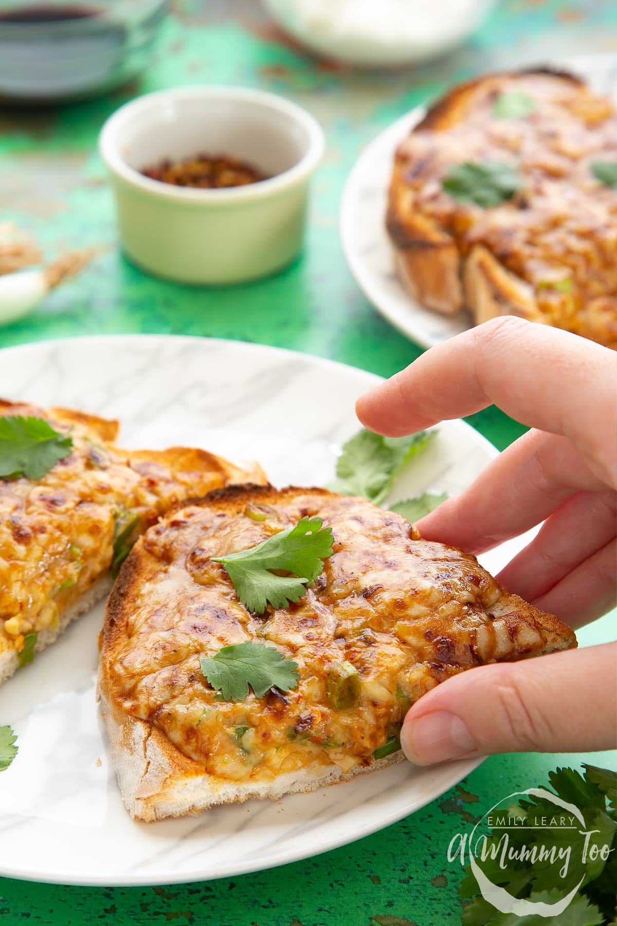 Two pieces of chilli cheese toast  on a white marbled plate, scattered with coriander. A hand reaches to take a piece.