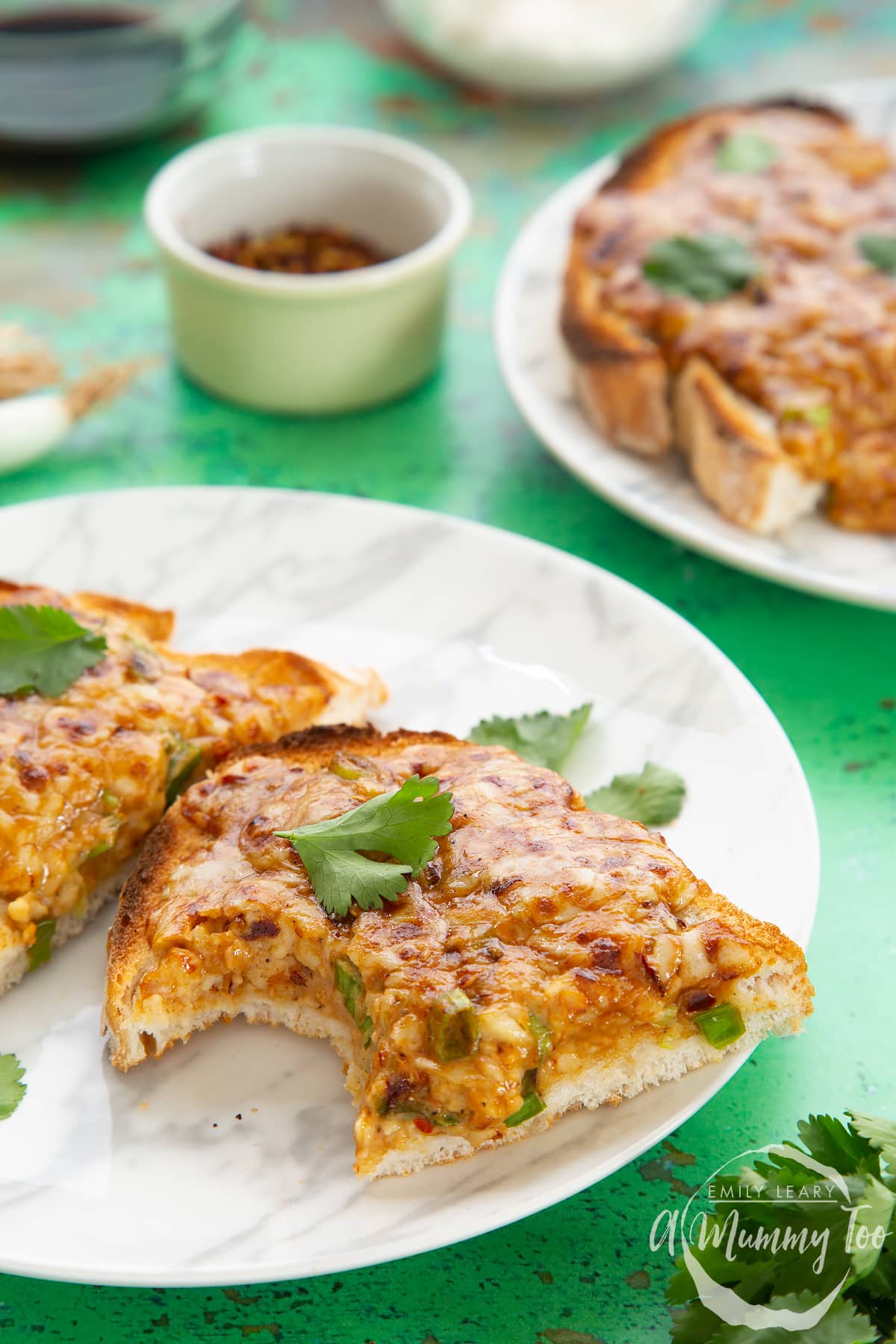 Two pieces of chilli cheese toast  on a white marbled plate, scattered with coriander. The piece in the foreground has a bite taken out of it.