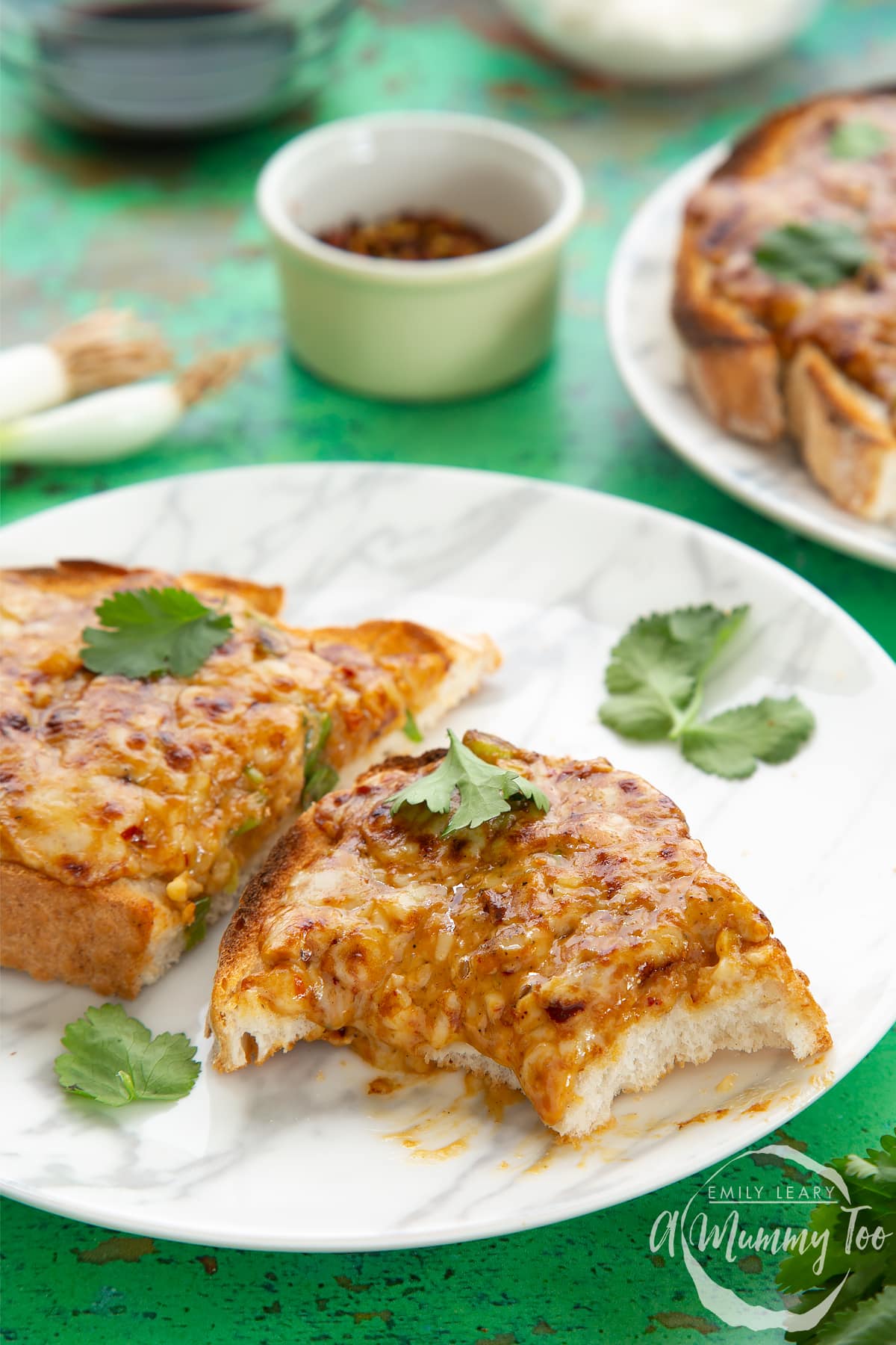 Two pieces of chilli cheese toast  on a white marbled plate, scattered with coriander. The piece in the foreground has several bites taken out of it.