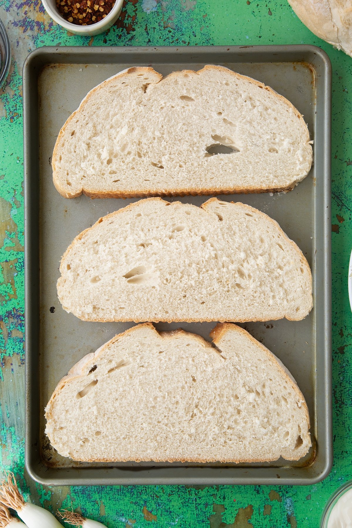 Three large slices of toast, turned onto their raw side on a baking tray. Ingredients to make chilli cheese toast surround the tray.