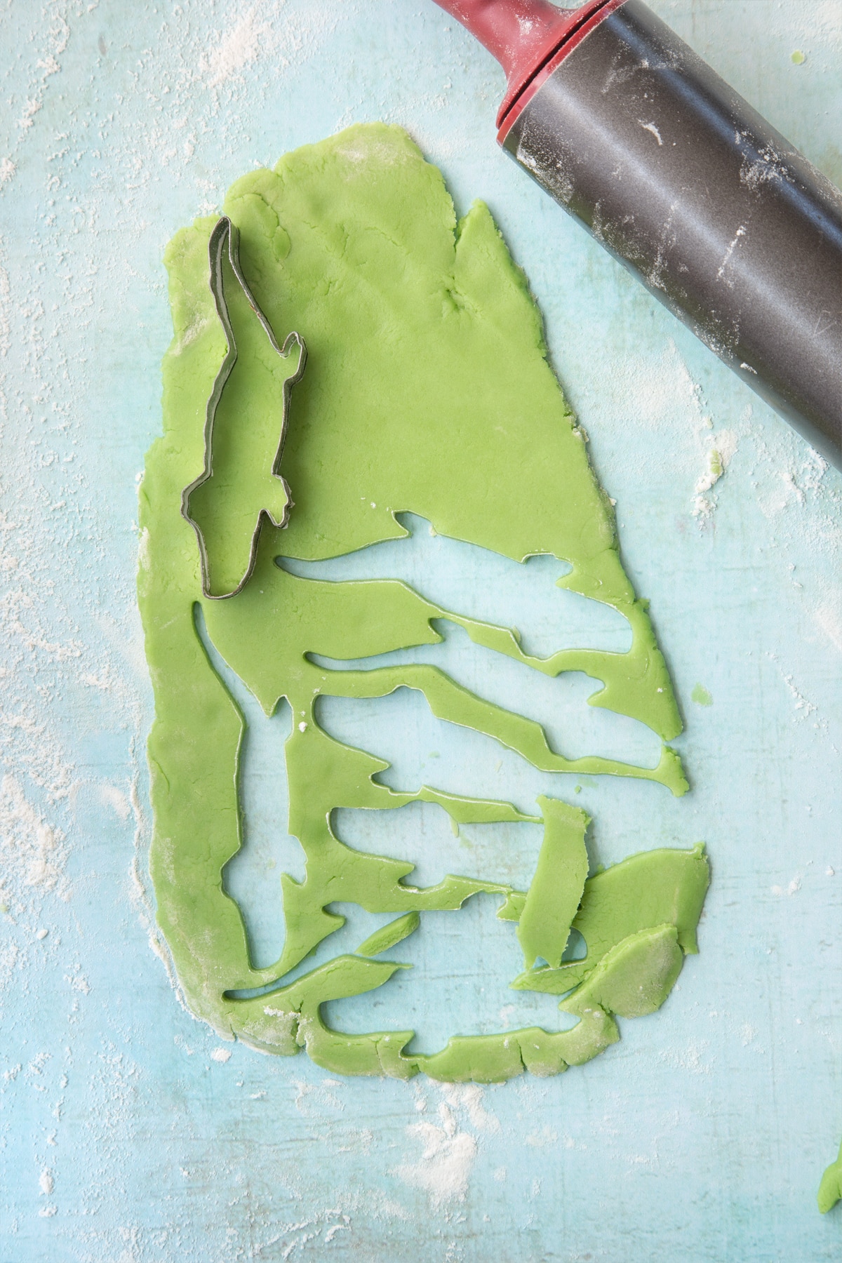 Dinosaur shaped cookie cutter cutting out from the green pastry.