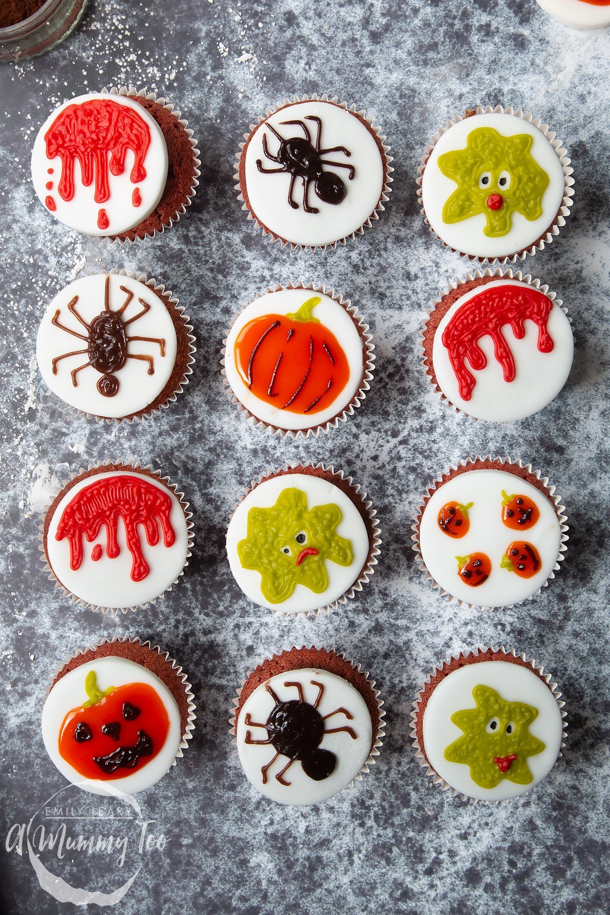 Dairy free Halloween cupcakes: red velvet cupcakes topped with chocolate frosting and white fondant discs decorated with icing pens. The cupcake are decorated with various designs, such as pumpkins, spiders. dripping blood and green monsters.