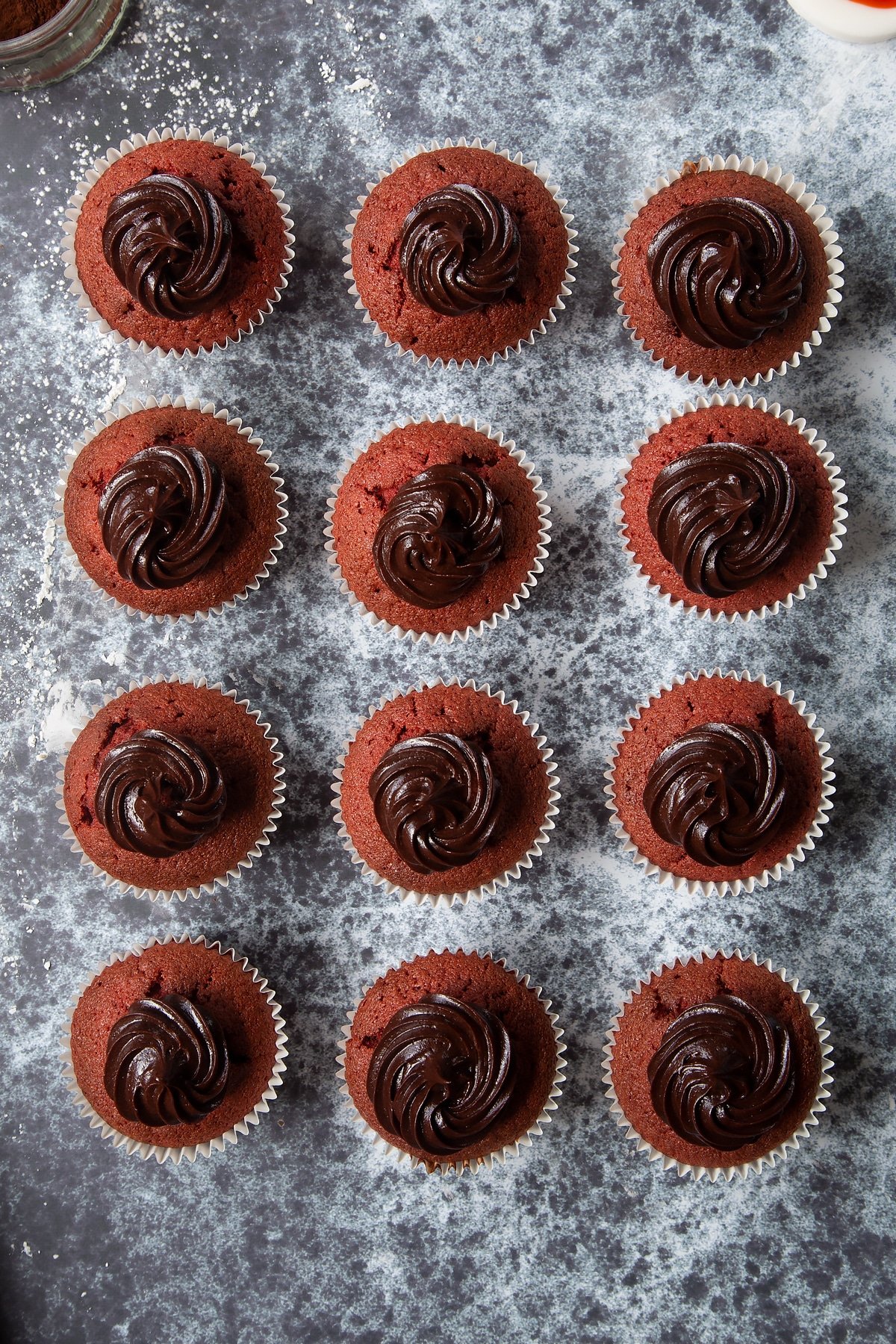 12 red velvet cupcakes toped with small swirls of chocolate frosting.
