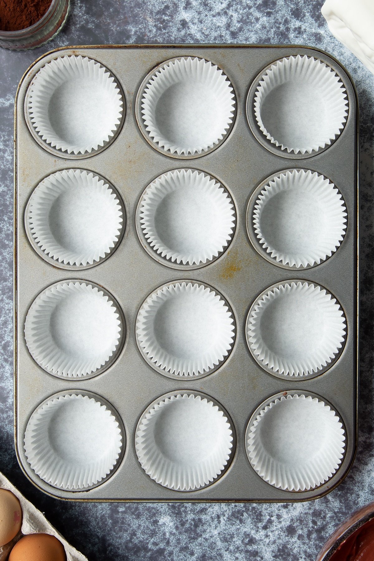12-hole muffin tray lined with cupcake cases. Ingredients to make dairy free Halloween cupcakes surround the tray.