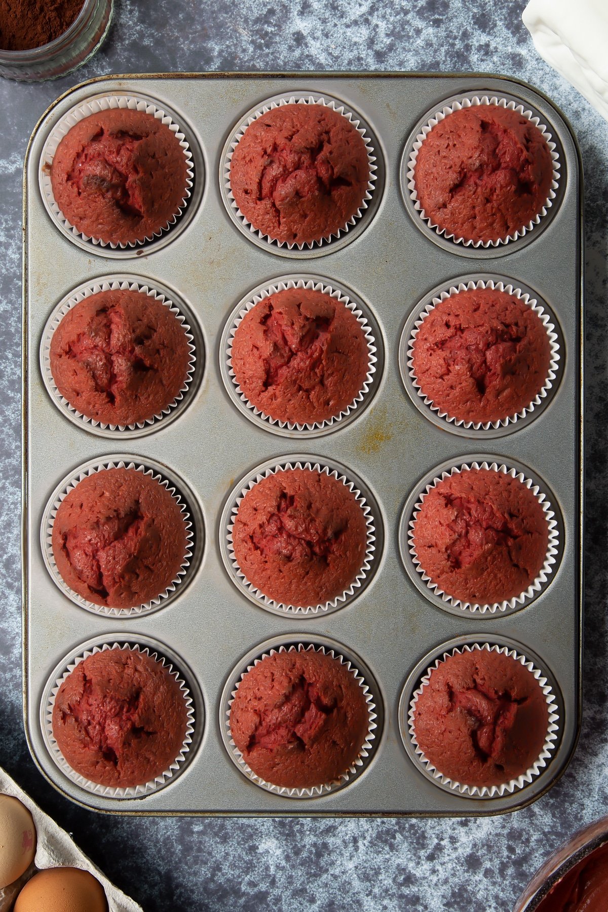 Dairy free red velvet cupcakes in a 12-hole muffin tray. Ingredients to make dairy free Halloween cupcakes surround the tray.