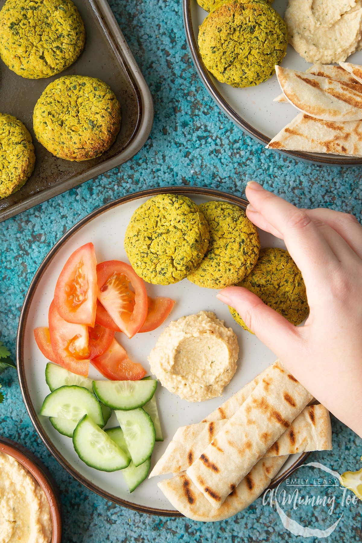 Gluten-free falafel on a plate with tomatoes, cucumber, hummus and griddled flatbread. A hand reaches for one.