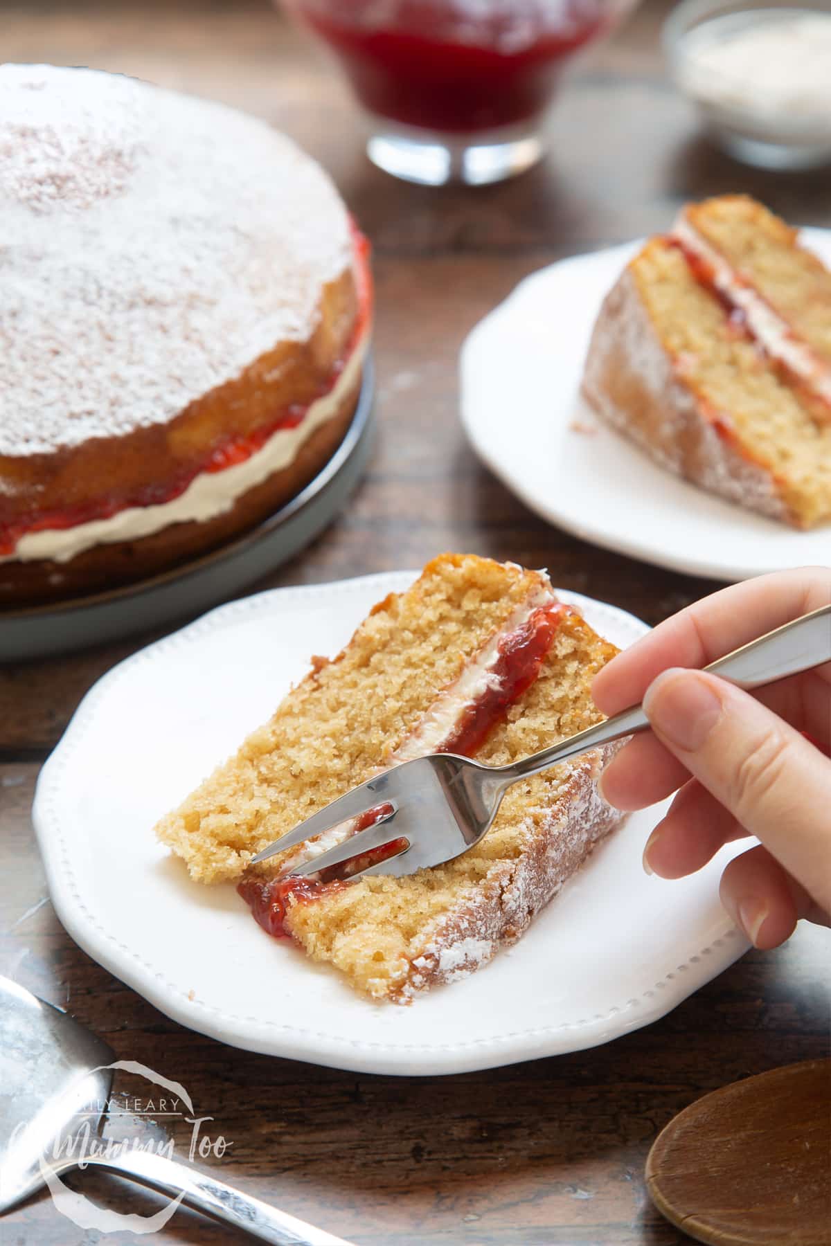 Overhead shot of a fork slicing a Golden sponge cake served on a white plate with a mummy too logo in the lower-left corner