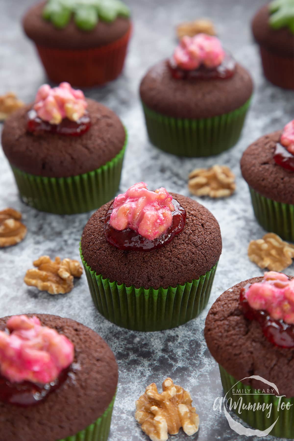 Gory Halloween cupcakes on a black background. The cupcakes are filled with jam and topped with pink candied walnuts that look like brains.