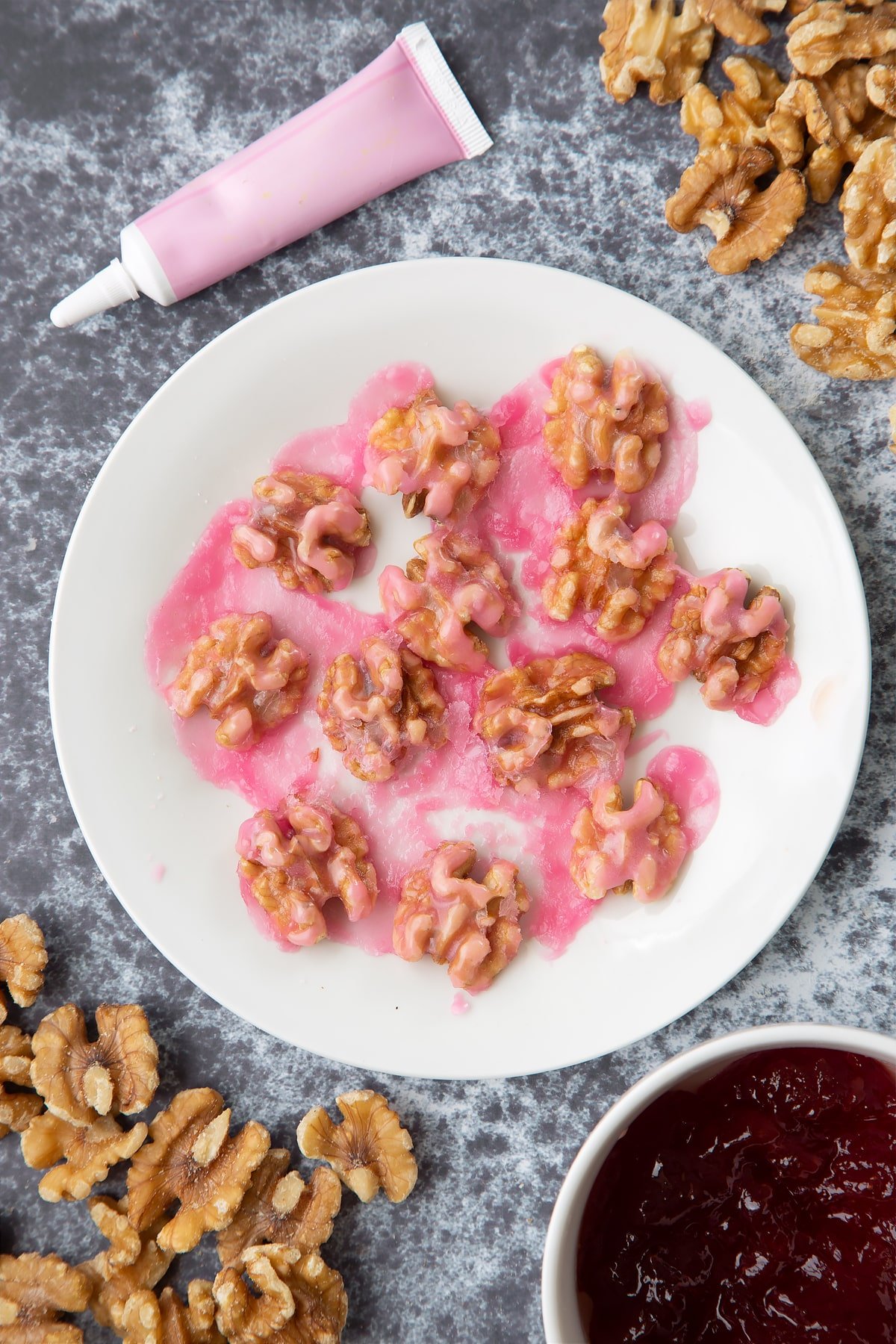 Walnuts on a white plate, glazed with melted pink icing. Ingredients to make gory Halloween cupcakes surround them.