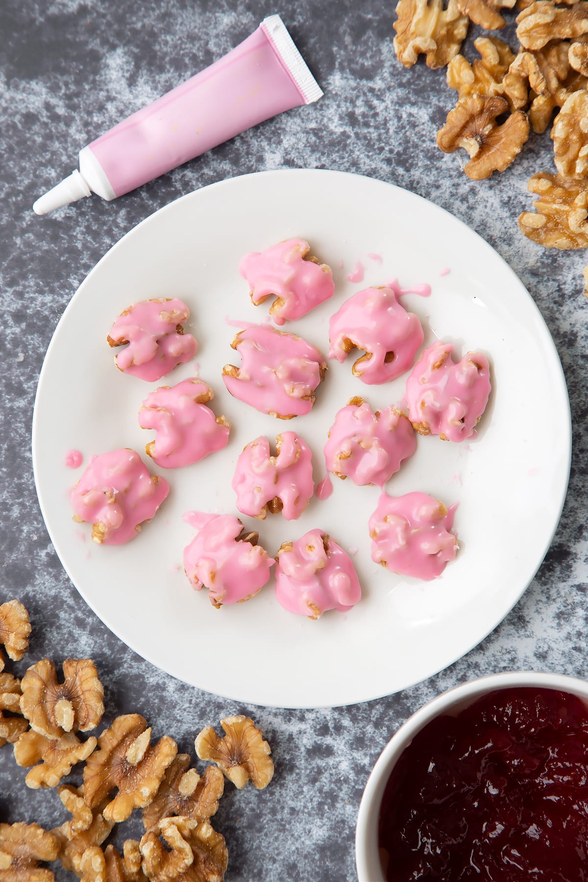 Walnuts on a white plate, painted with pink icing. Ingredients to make gory Halloween cupcakes surround them.