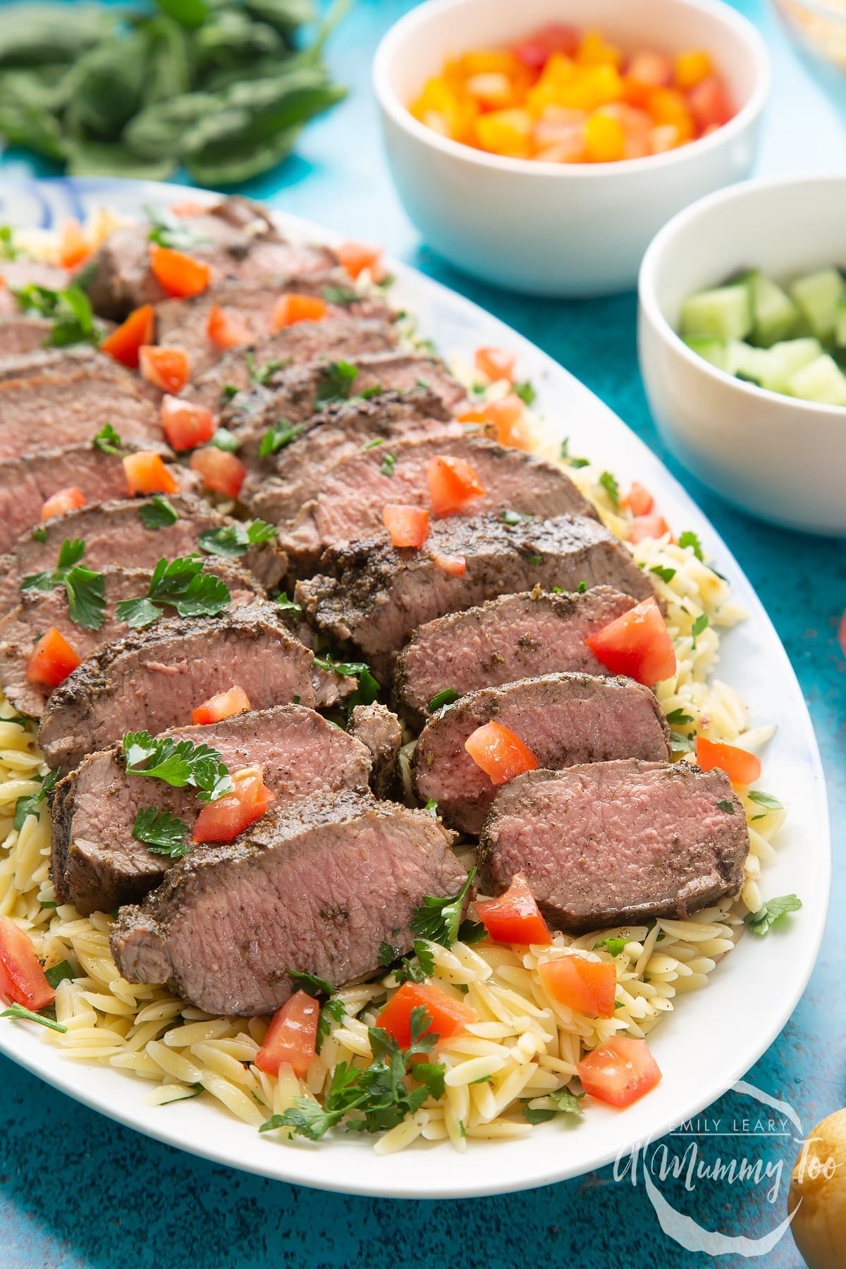 Slices of herby lamb arranged on a bed of orzo on an oval platter. 