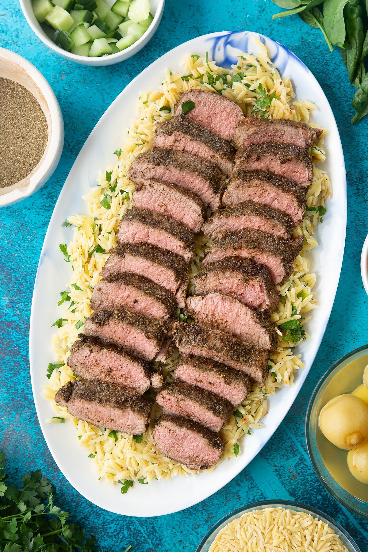 Lemony orzo spread on an oval platter, topped with slices of herby lamb.