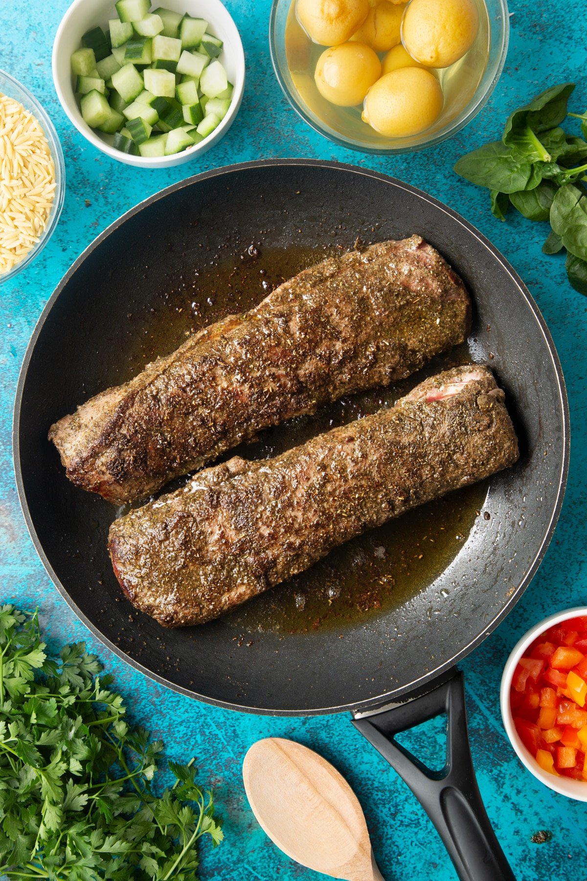 Two pieces of cooked cannon of Welsh lamb covered with a herb and oil rub in a frying pan. 