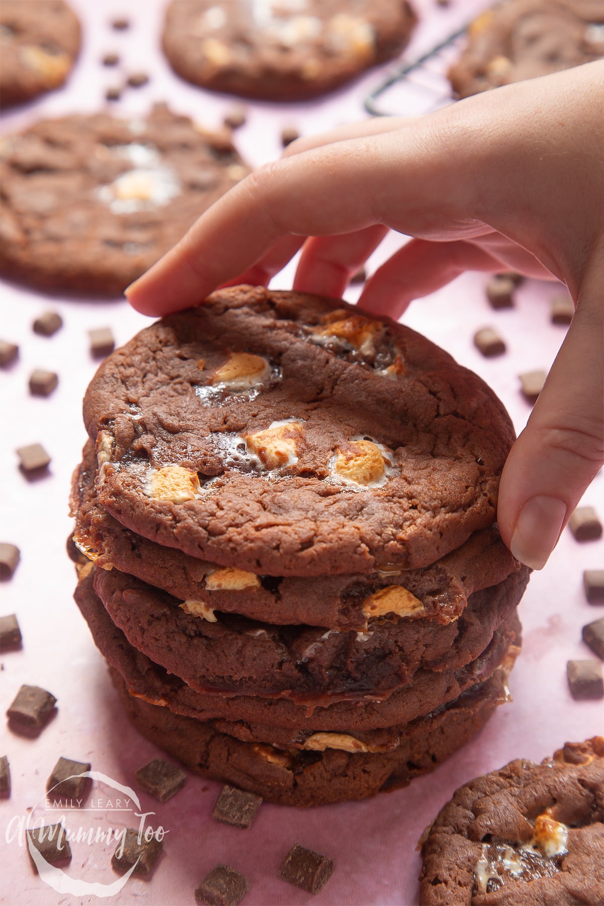 Front view shot of a hand holding a stack of ultimate marshmallow cookie with a mummy too logo in the lower-left corner