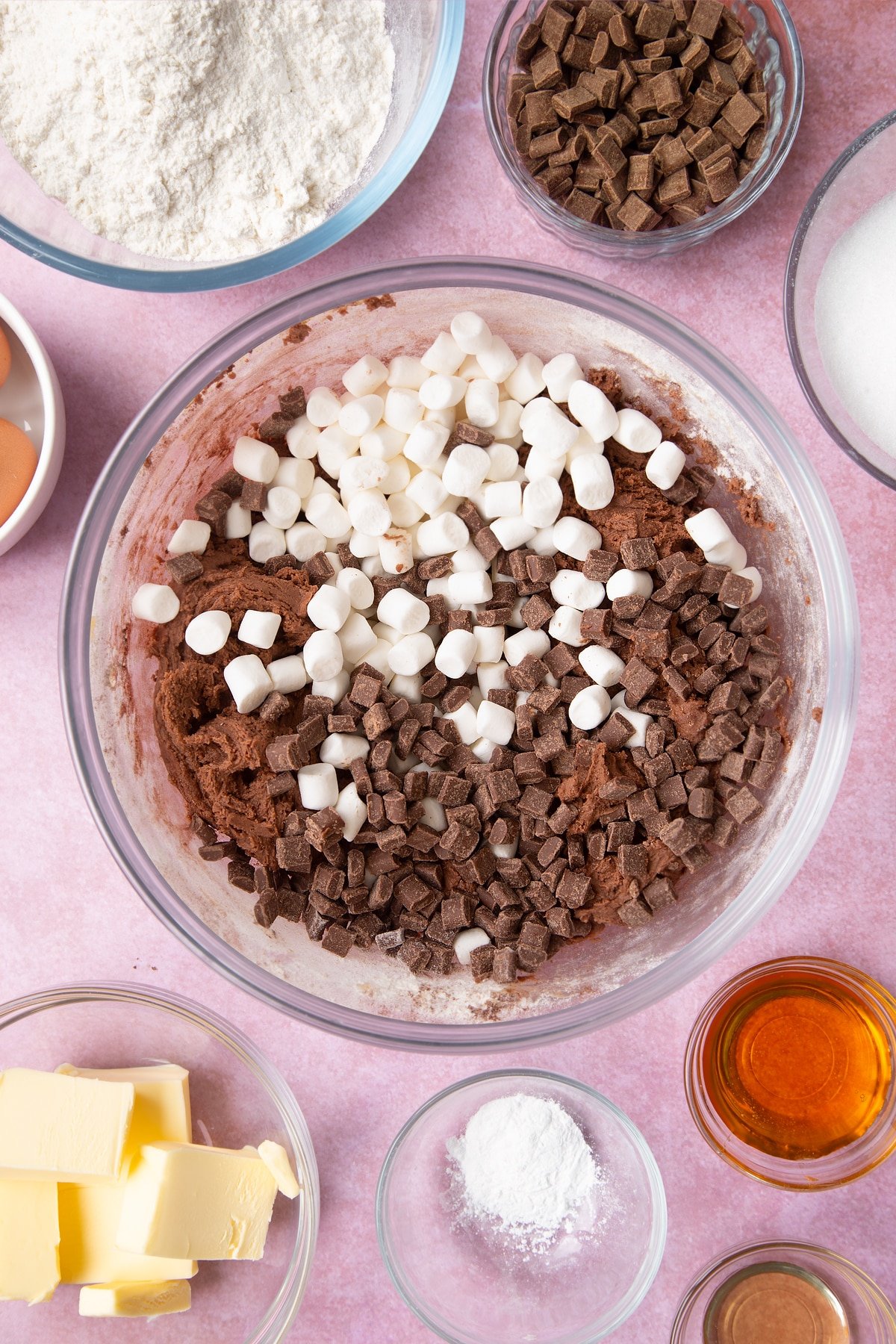 Overhead shot of chocolate cookie dough, marshmallows and chocolate chips in a large clear bowl