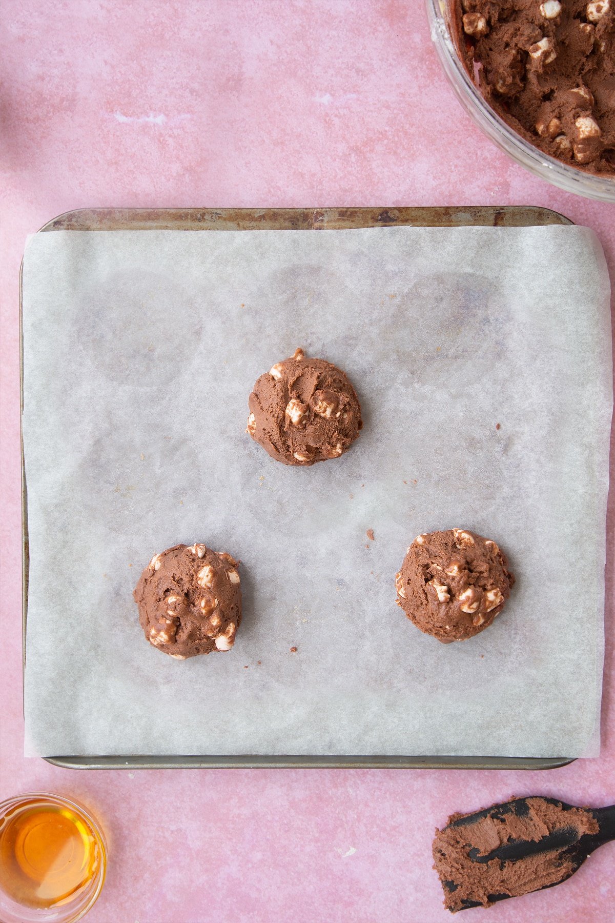 Overhead shot of 3 cookie dough balls on a lined baking tray