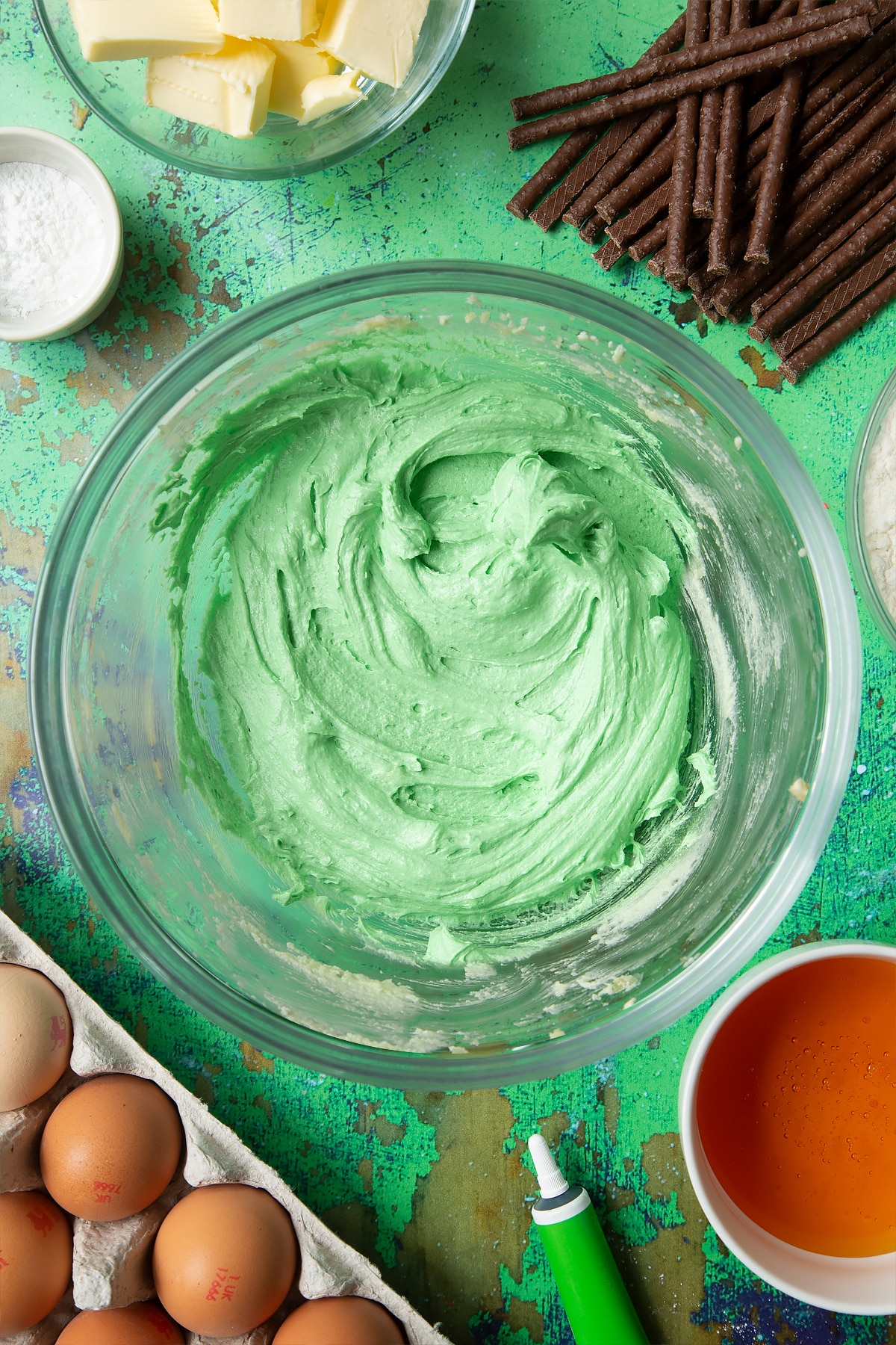 Creamed butter, sugar and green food colouring in a mixing bowl. Ingredients to make Matchmaker cookies surround the bowl.