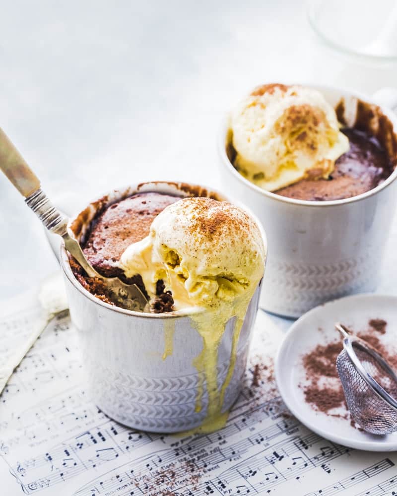 Two Nutella mug cakes topped with vanilla ice cream.