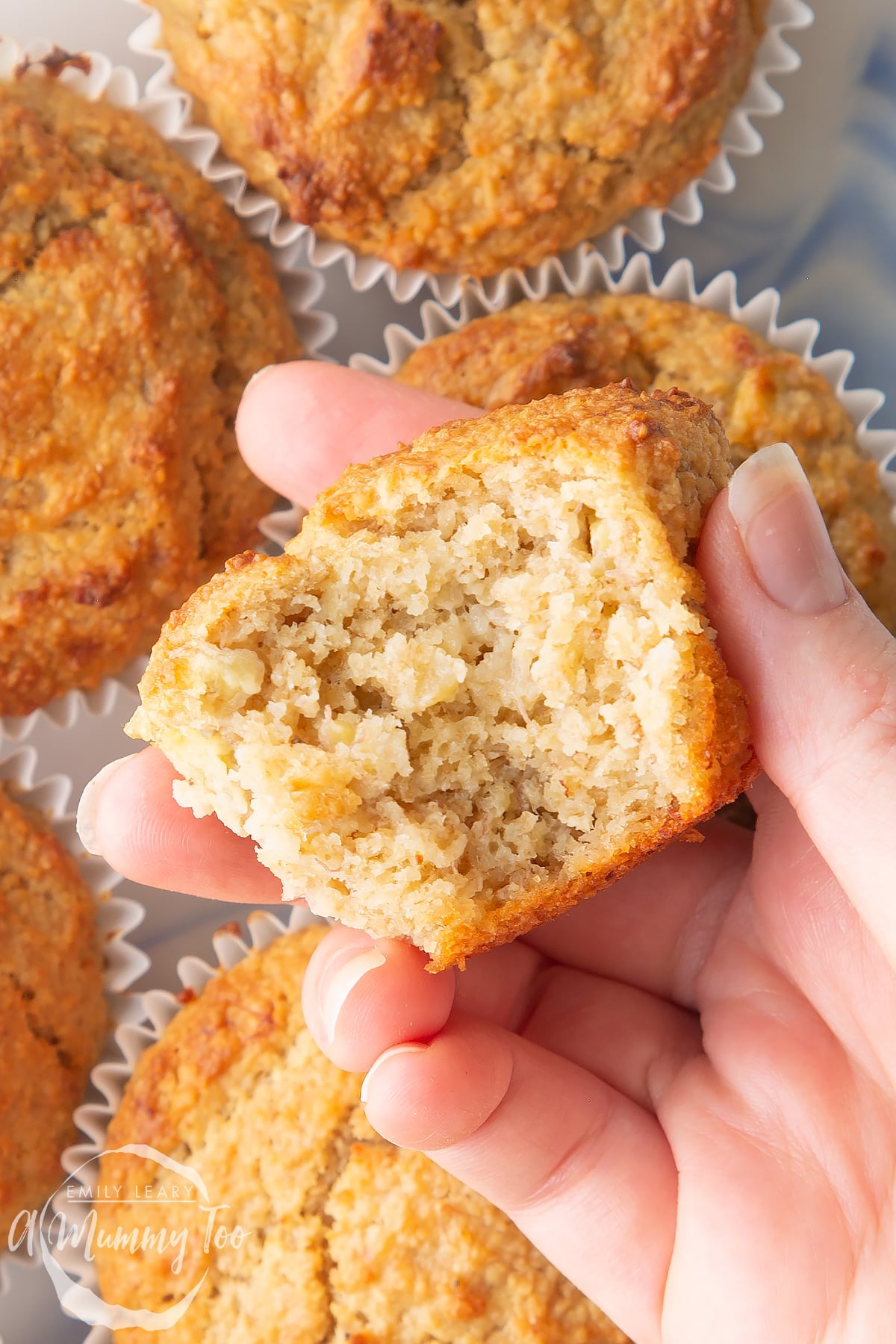 Front angle shot of a hand holding a half eaten breakfast muffin with a mummy too logo in the lower-left corner