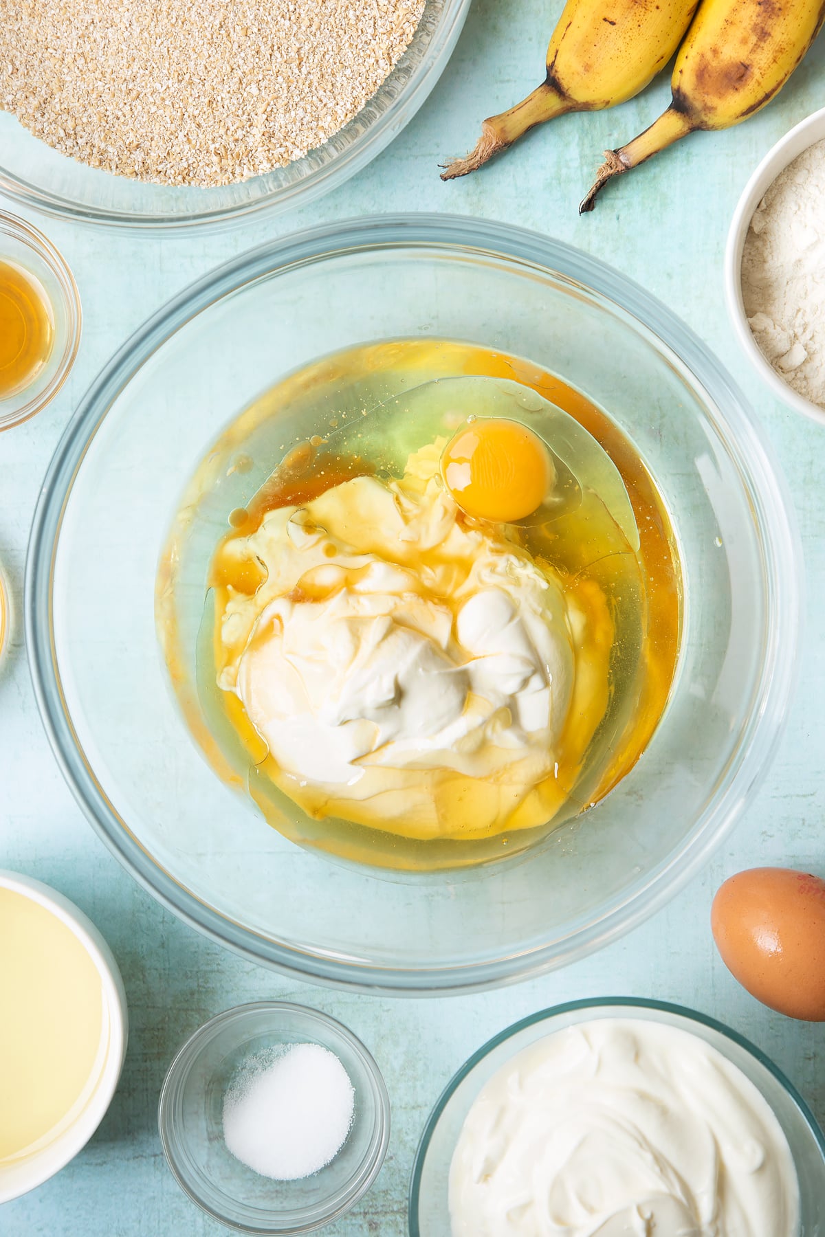 Overhead shot of oil, honey, plain yogurt and eggs in a clear large mixing bowl