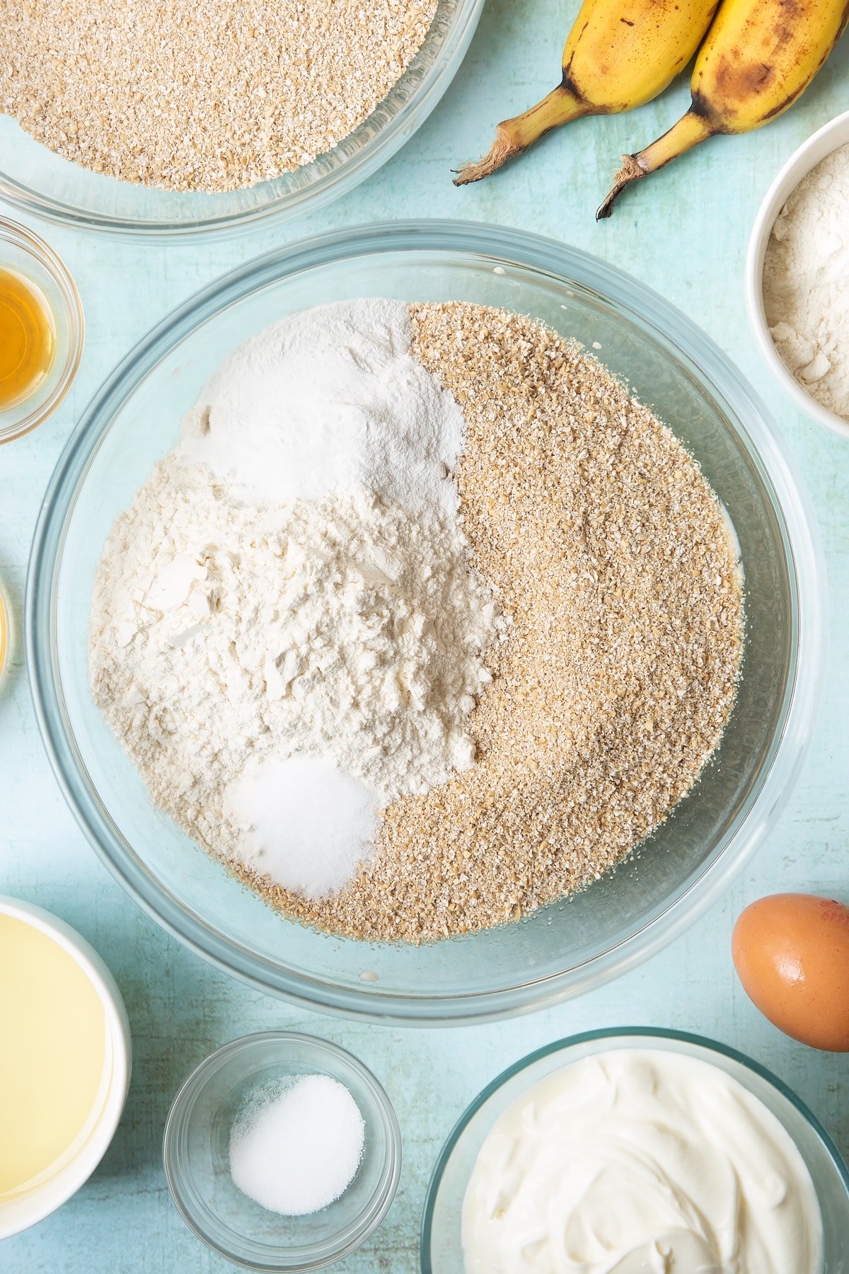 Overhead shot of oat bran, plain flour, baking powder and salt in a large clear bowl