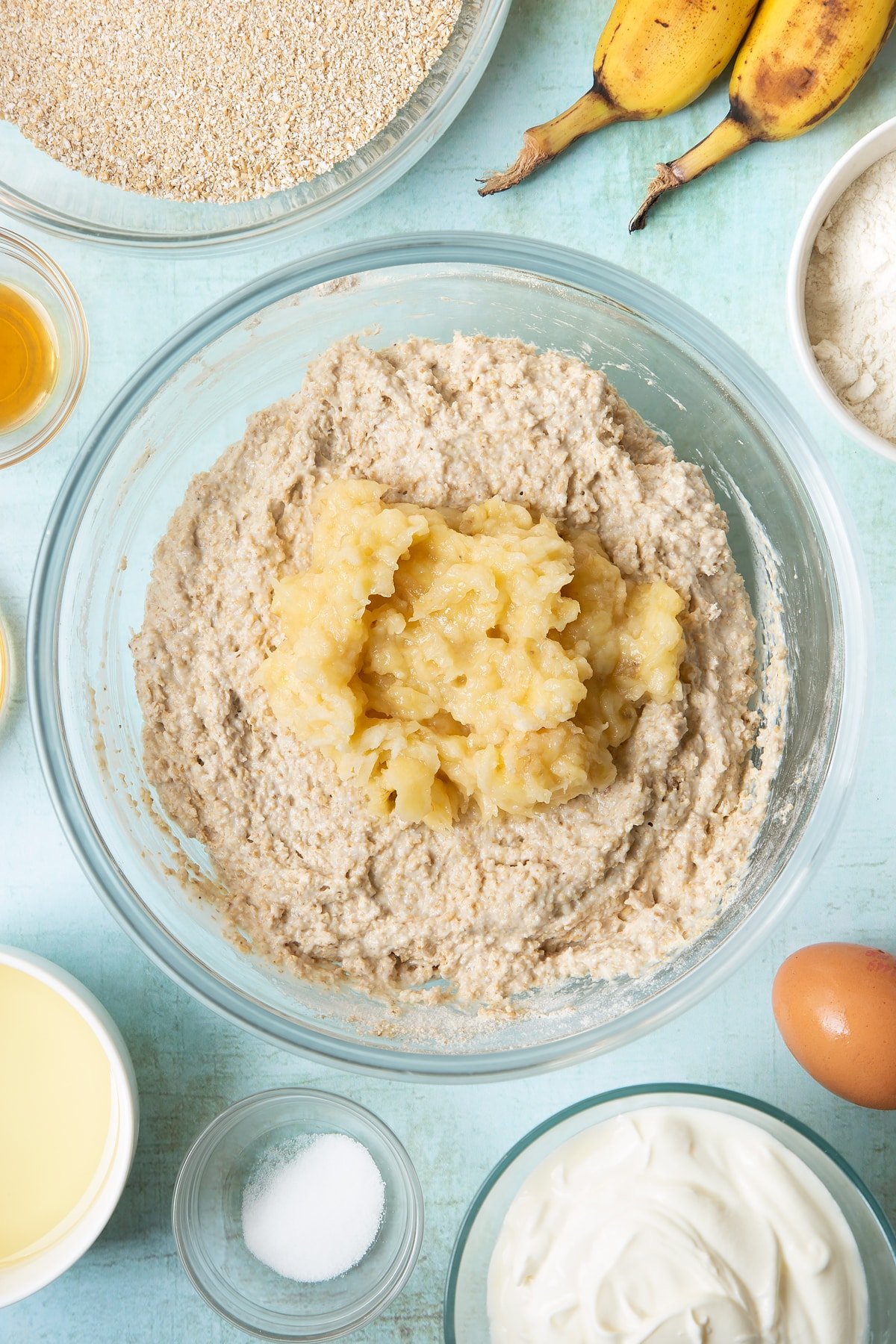 Overhead shot of muffin mix with banana on top in a clear bowl