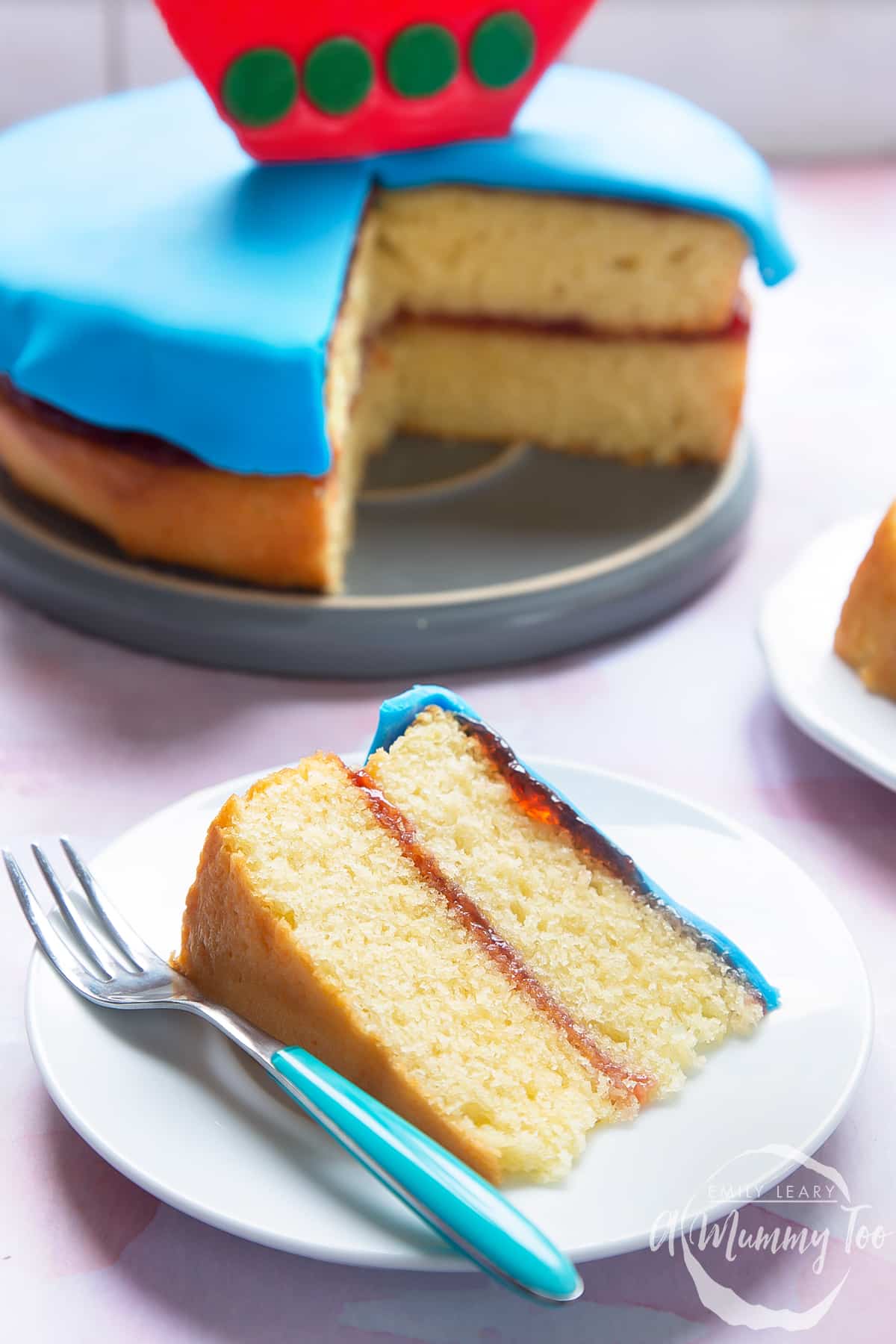 A close up slice of the sailboat cake on a white decoative plate with a cake fork on the side.