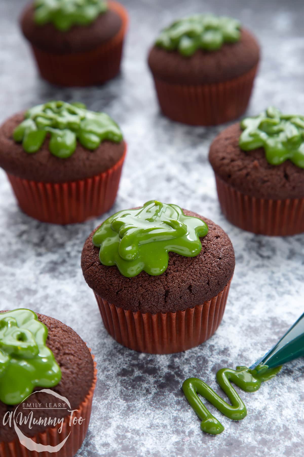 Slime cupcakes on a black backdrop. The cakes have a chocolate sponge topped with dyed-green caramel.