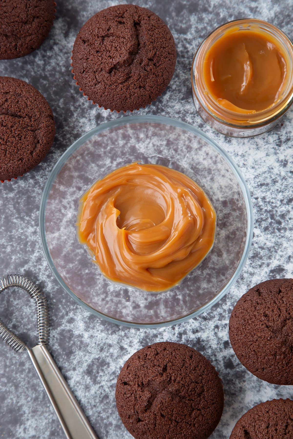 A small glass bowl of caramel. Chocolate cupcakes surround the bowl.