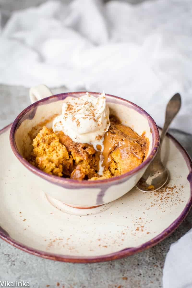 Spiced pumpkin molten mug cake in a cup on a saucer. The cake is topped with ice cream.