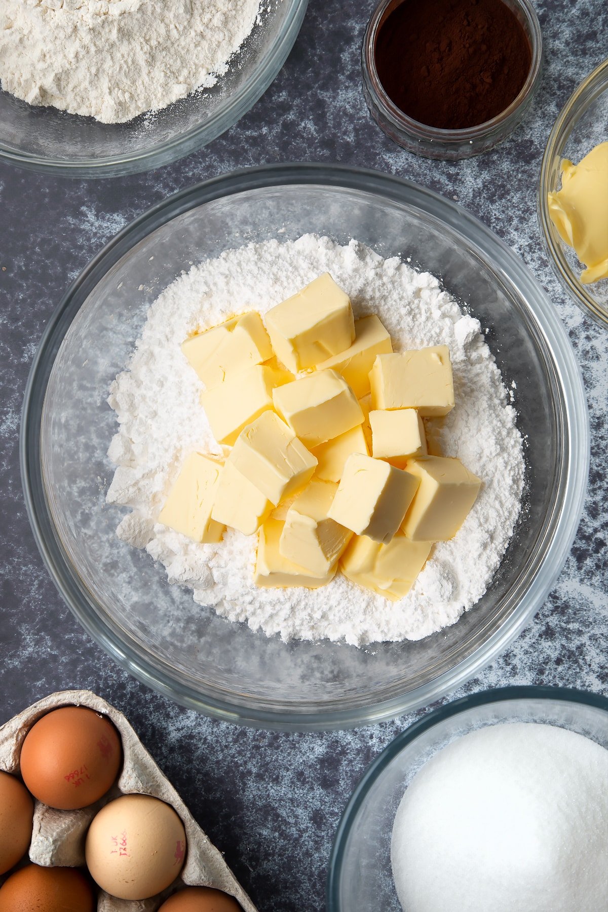 Icing sugar, vanilla and butter in a large mixing bowl. Ingredients to make spider web cupcakes surround the bowl.