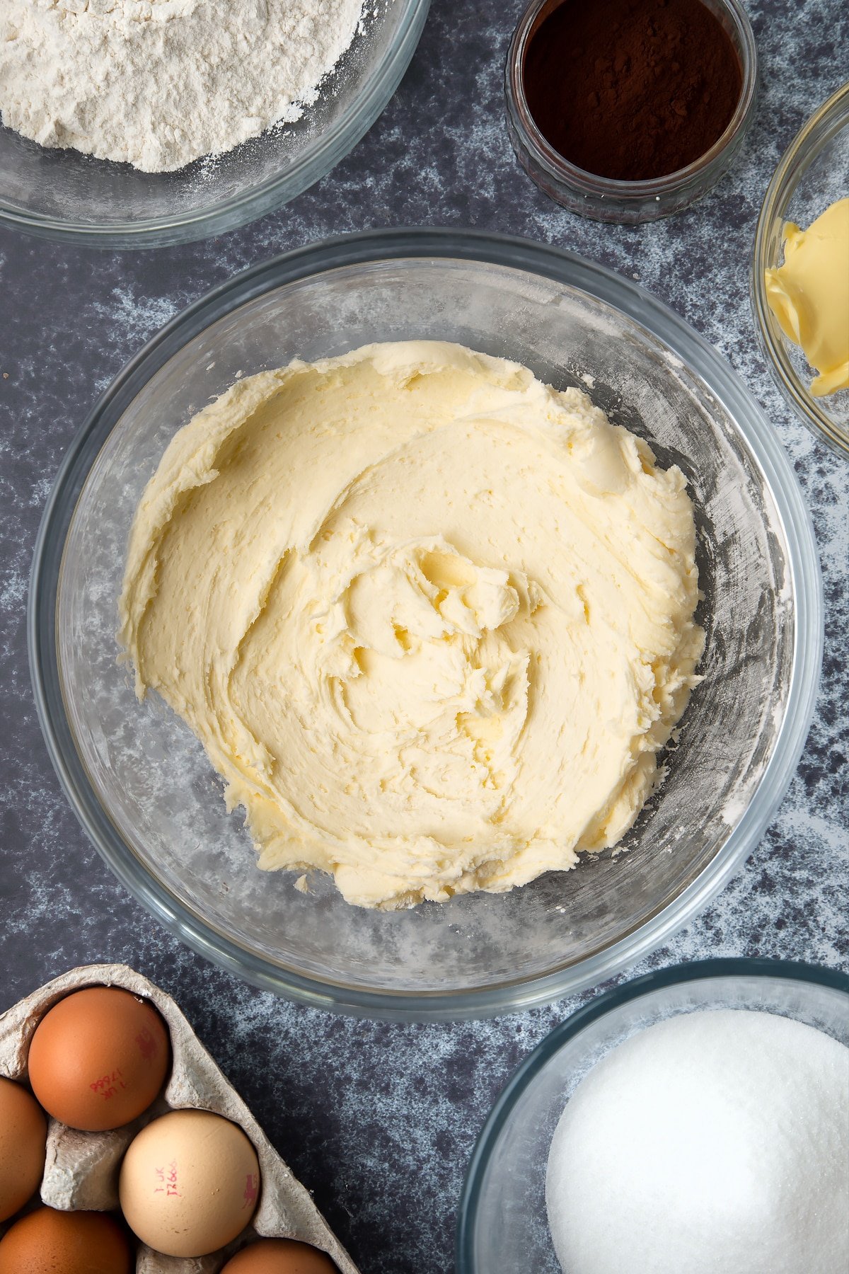 Icing sugar, vanilla and butter whisked together in a large mixing bowl. Ingredients to make spider web cupcakes surround the bowl.
