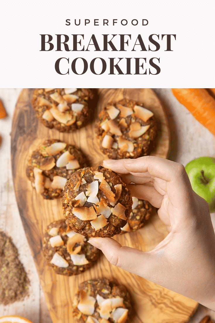 Front angle shot of a hand holding a breakfast cookie topped with coconut shavings above graphic text SUPERFOOD BREAKFAST COOKIES