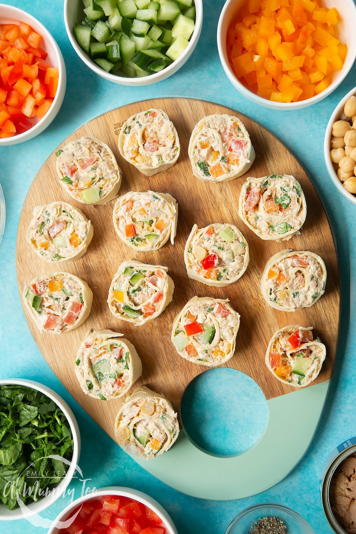 Tuna pinwheels on a wooden board, surrounded by fresh fruit and veg.