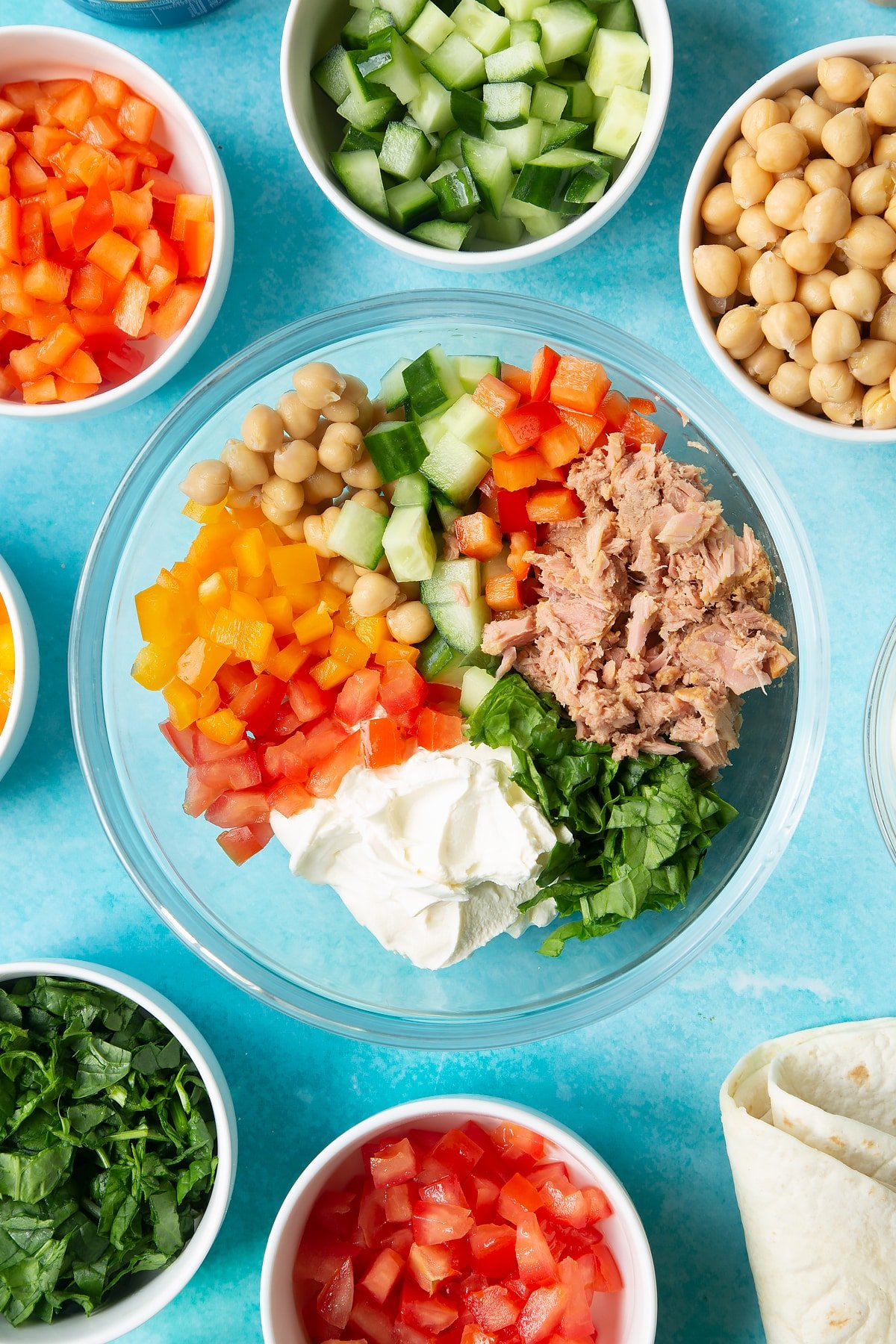 Cream cheese, tuna and veg in a bowl. Ingredients to make tuna pinwheels surround the bowl.