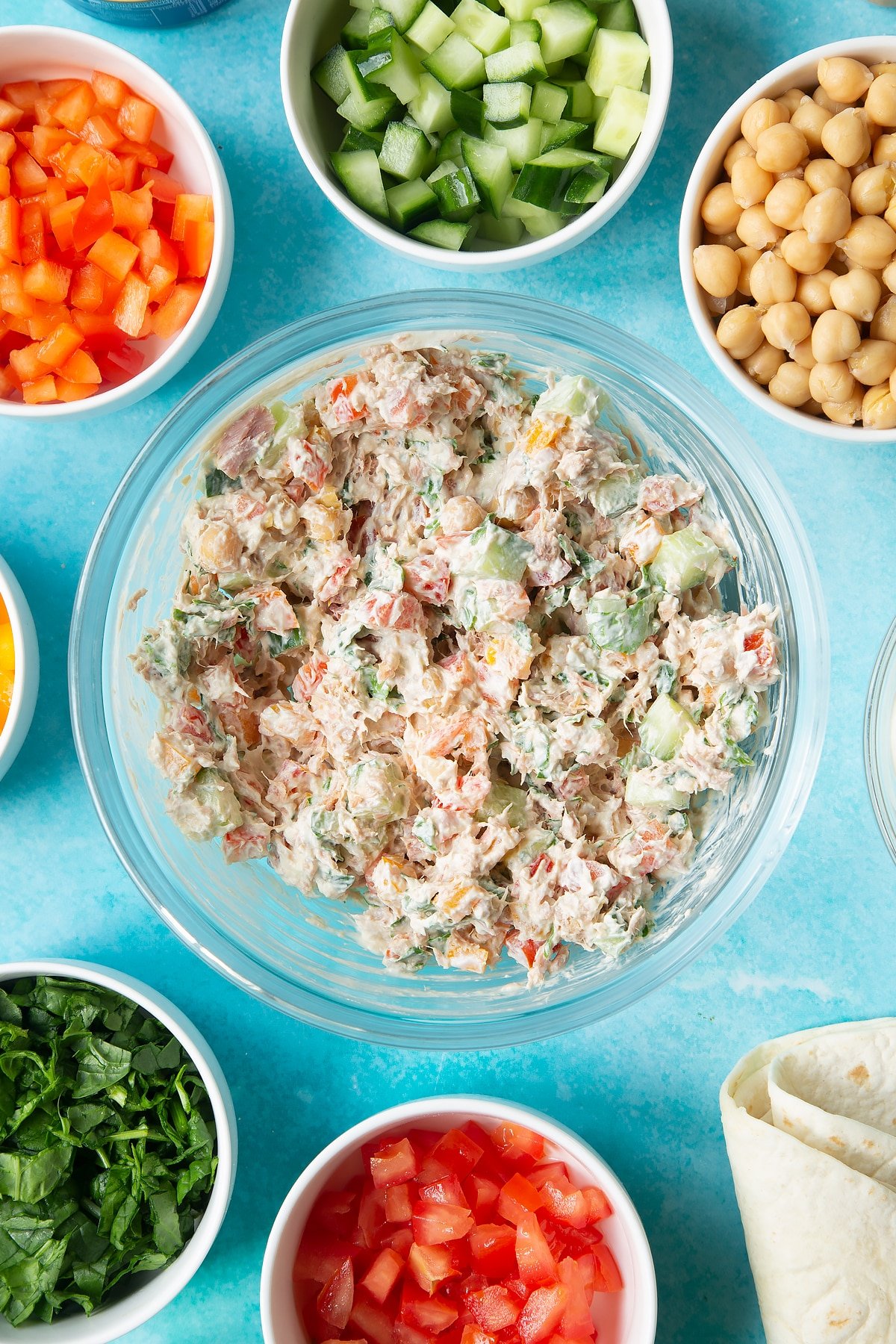 A mix of cream cheese, tuna and veg in a bowl. Ingredients to make tuna pinwheels surround the bowl.