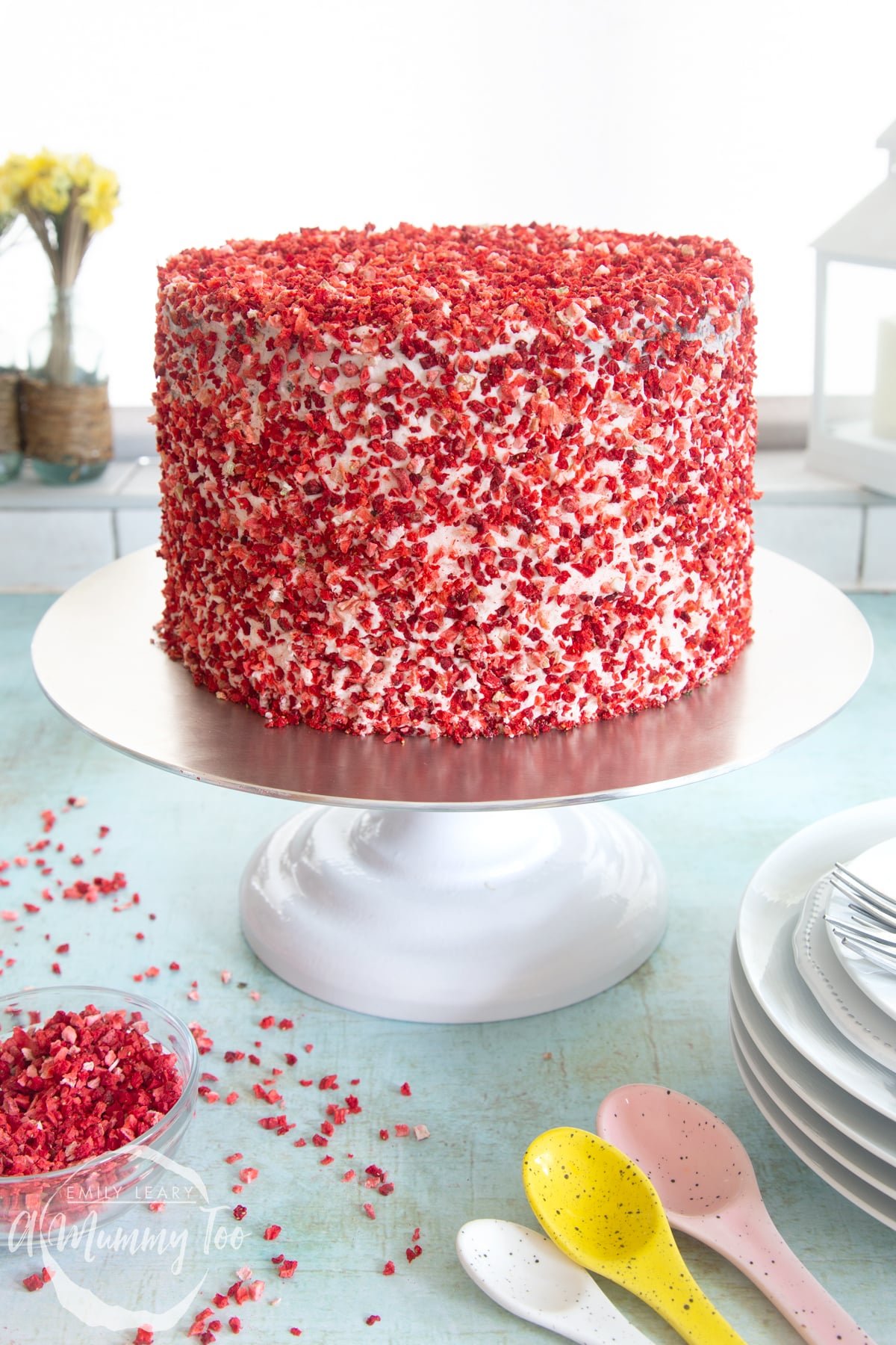 A pink ombre cake on a cake stand. The cake is covered with pale pink frosting and freeze dried strawberry pieces.