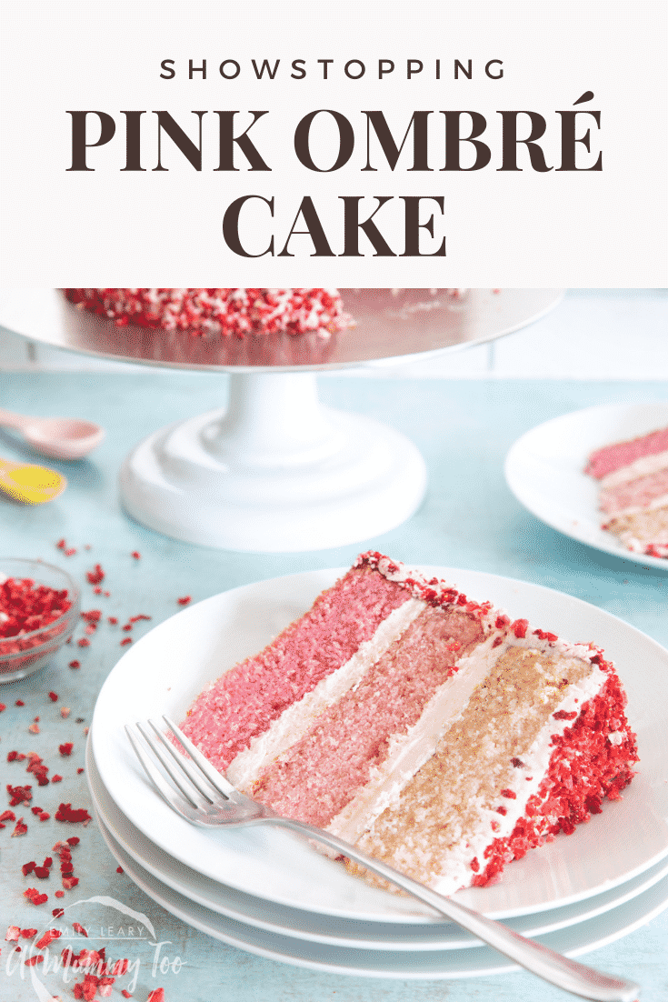 A slice of pink ombre cake on a stack of small white plates. The cake has three layers, each an increasingly intense shade of pink. The sponges are layered with pale pink frosting and the outside is decorated with freeze dried strawberry pieces. A fork rests on the plate. Caption reads: showstopping pink ombre cake